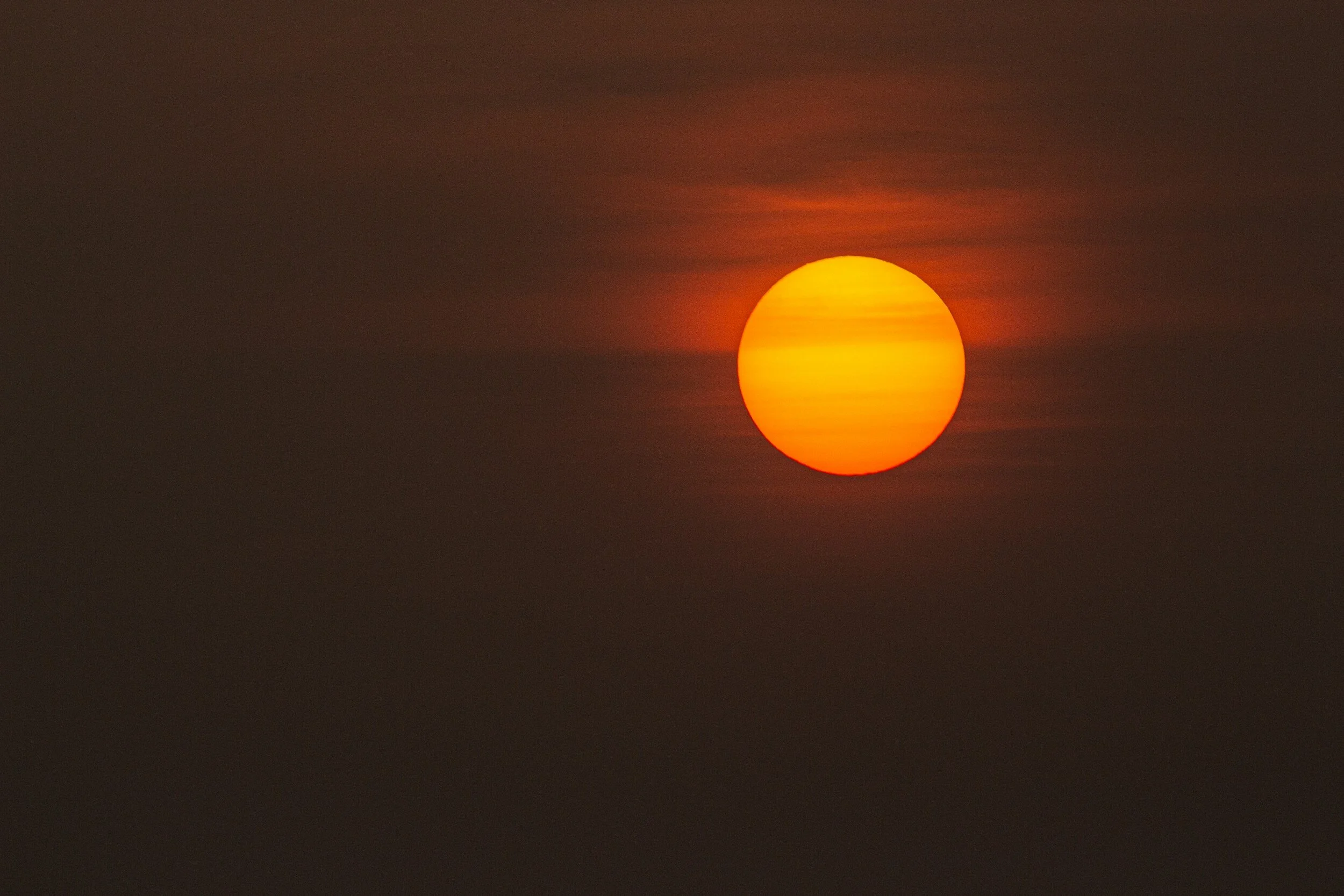 A bright orange and yellow sun in a dark sky with faint clouds.