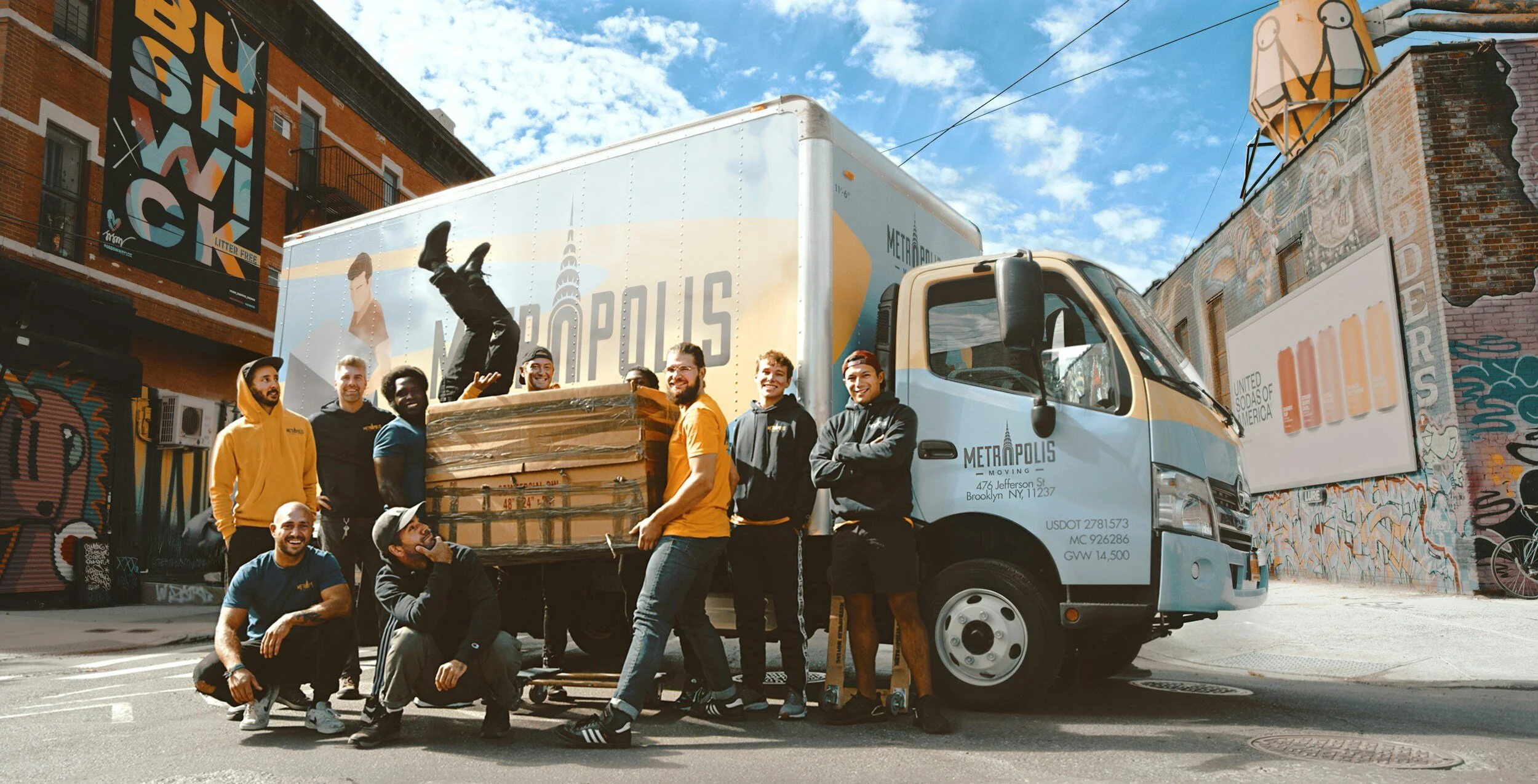Team of movers with a moving truck in front of colorful urban murals, loading furniture in a city street.