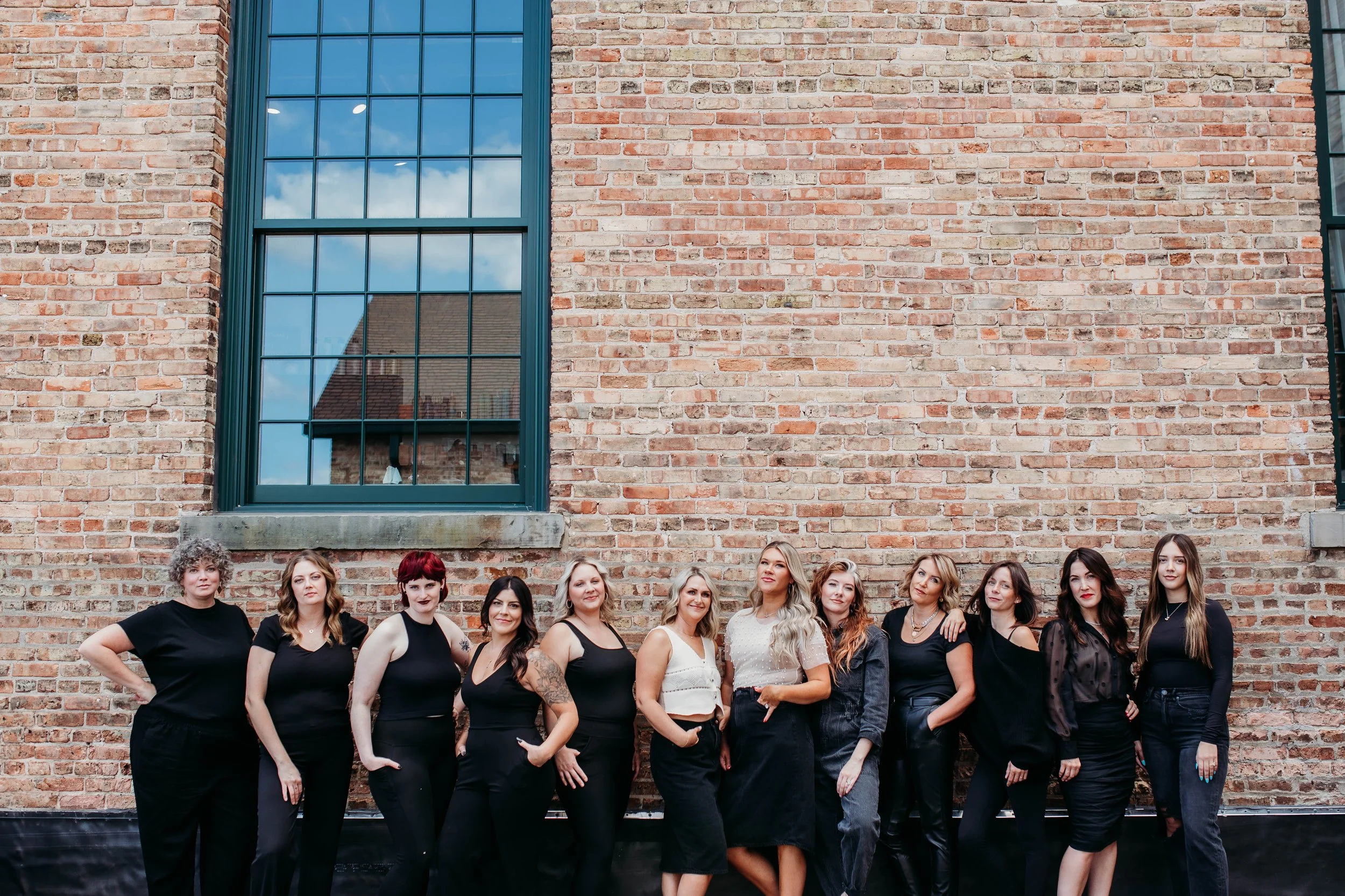 Group of women standing in front of a brick building with large windows, posing for a photo.