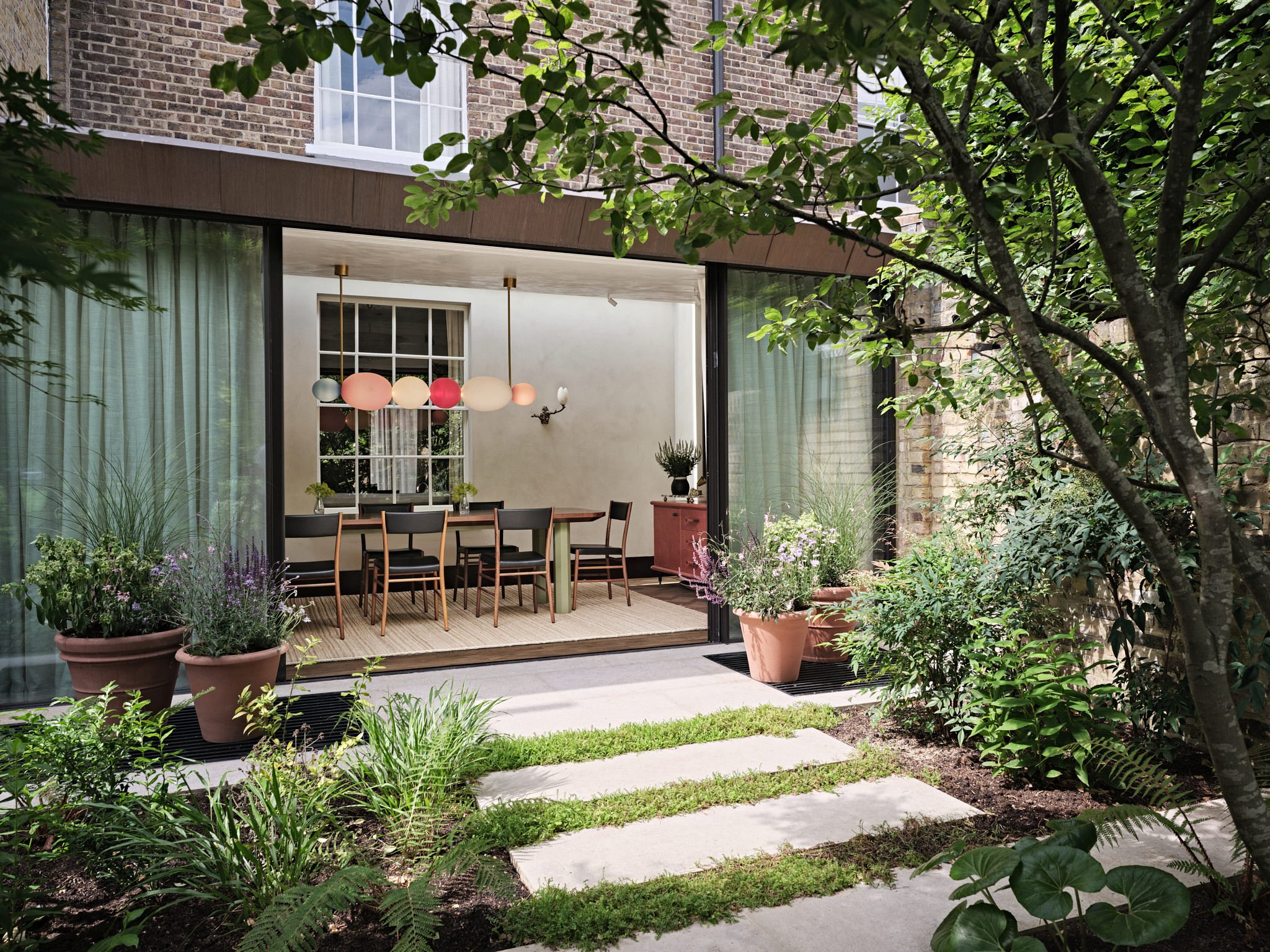 View of glass extension in modern London house from leafy garden with path, designed by Bryan O'Sullivan Studio and architecture by Tom Rutt