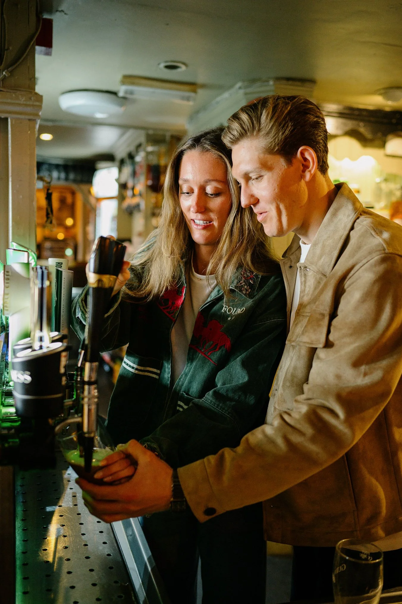 Newly engaged couple laughing as they pour their first pint of Guinness together behind the bar at McDermott's pub in Doolin, County Clare
