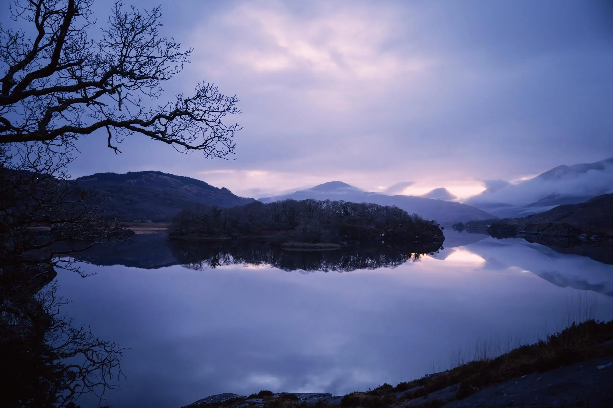Handheld evening shot of Killarney lakes from Molls Gap road, showing mountain silhouettes and a perfect water reflection.
