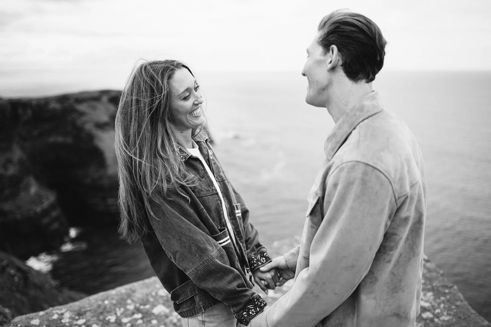Newly engaged couple laughing together at Hag's Head, Cliffs of Moher, County Clare, with the Atlantic behind them, black and white