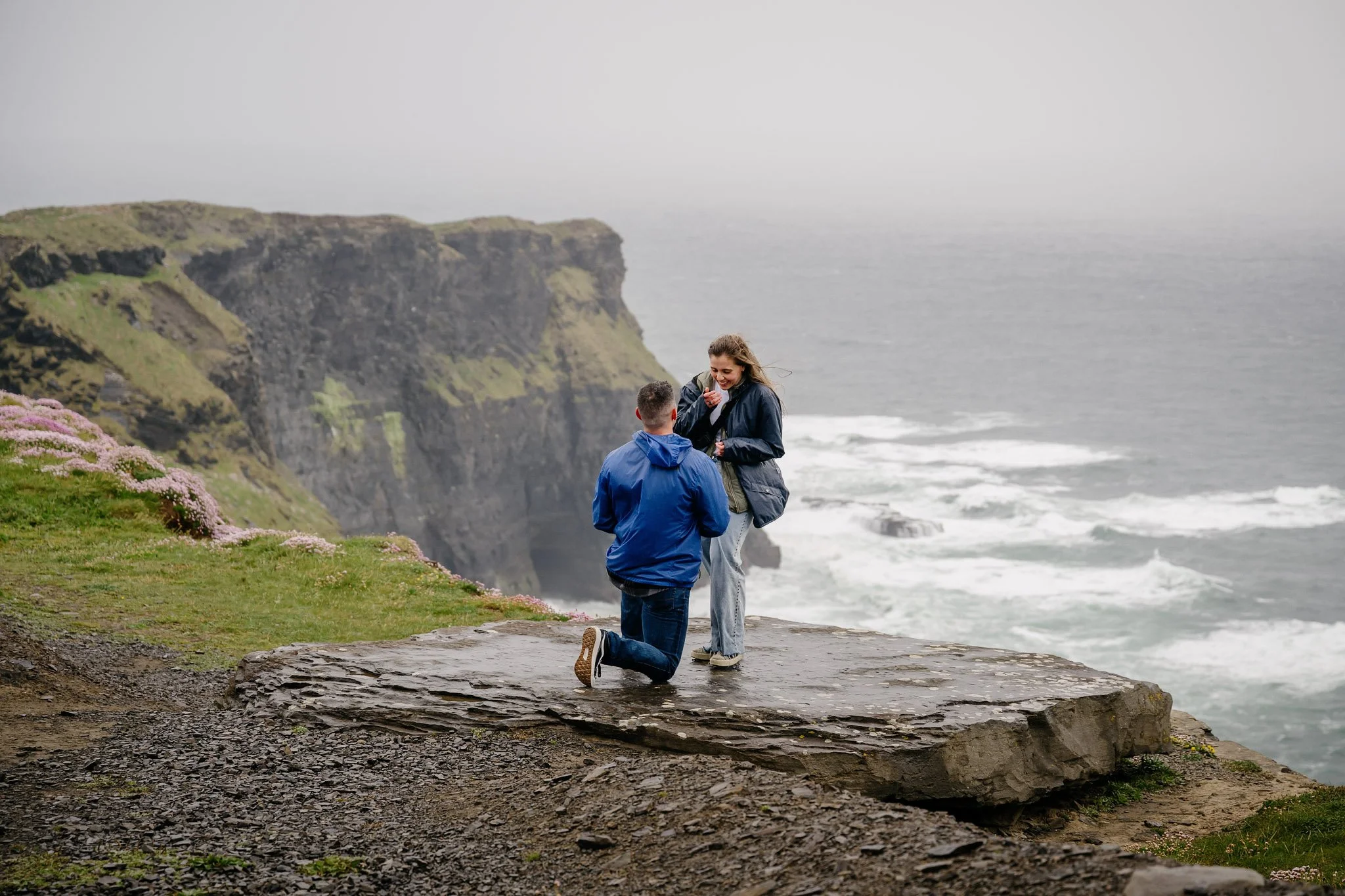 Man proposing on one knee on a misty, wild day at Hag's Head, Cliffs of Moher, with sea thrift on the cliff edge and rough Atlantic surf below