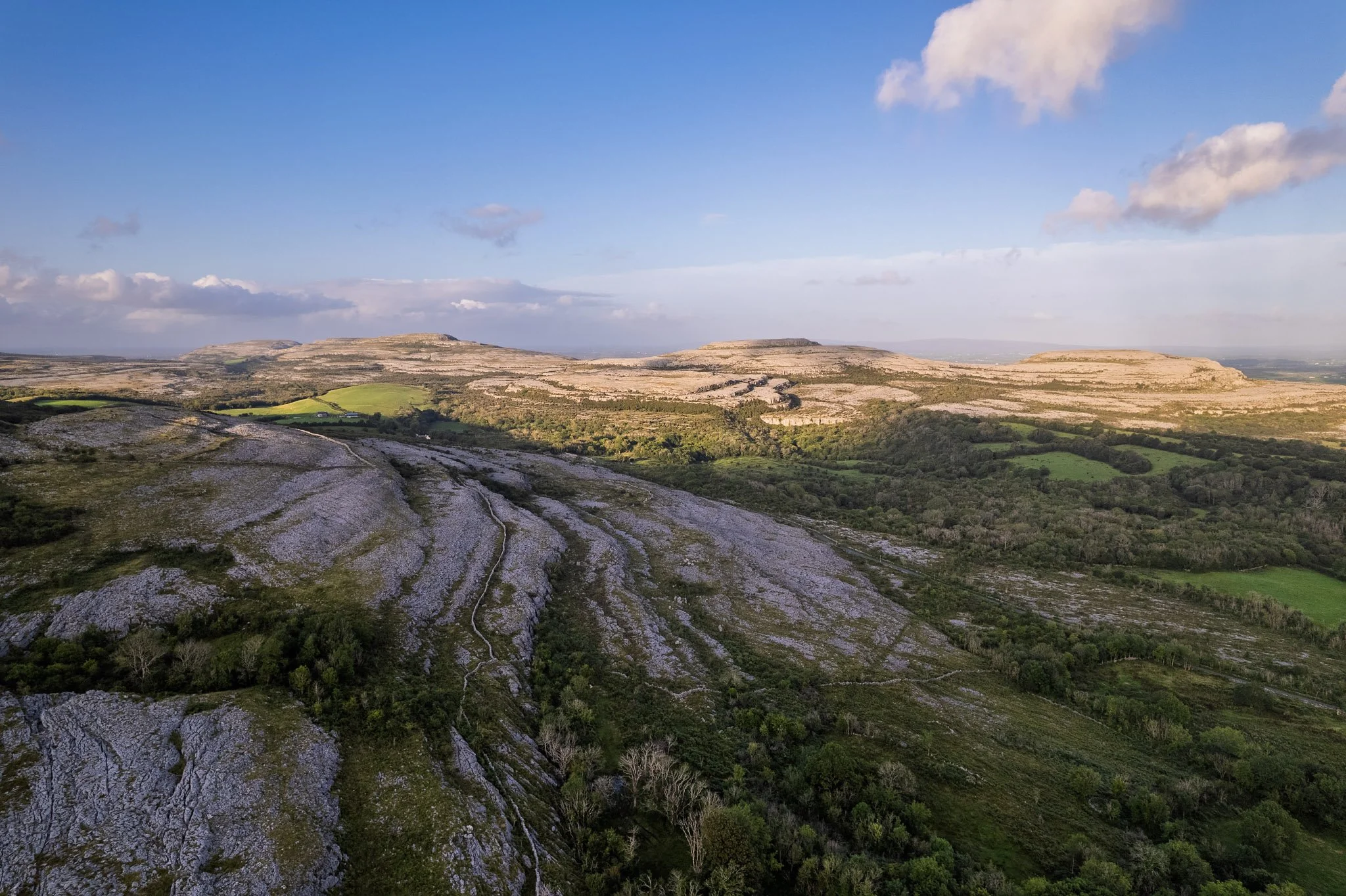 Golden evening light over the limestone terraces and hills of the Burren from Fahee North viewpoint near Carron, County Clare