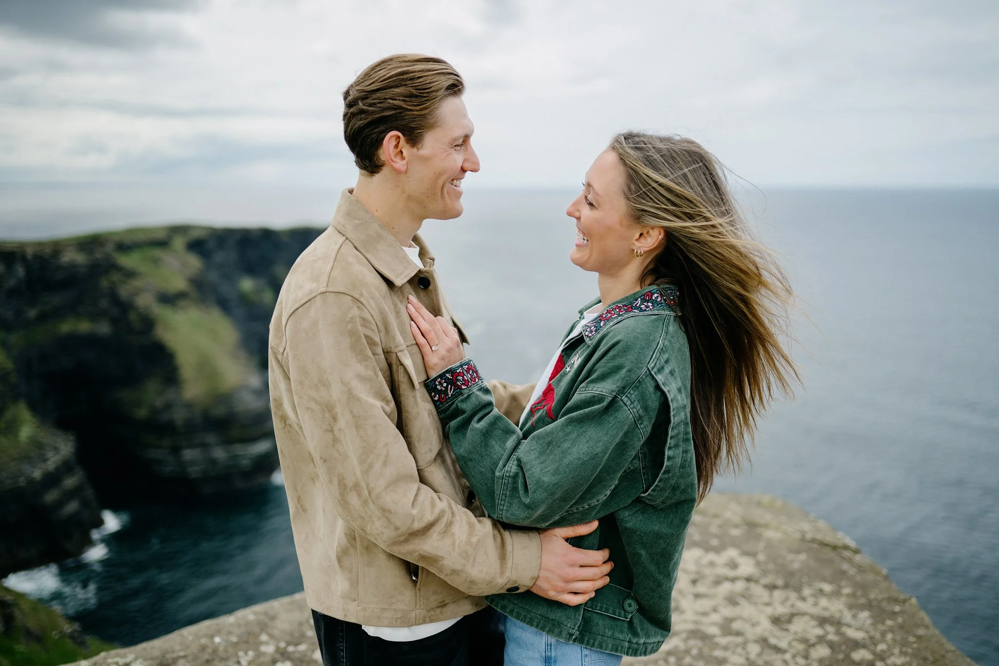 Newly engaged couple laughing together at Hag's Head, Cliffs of Moher, County Clare, the woman's engagement ring visible with the Atlantic behind them