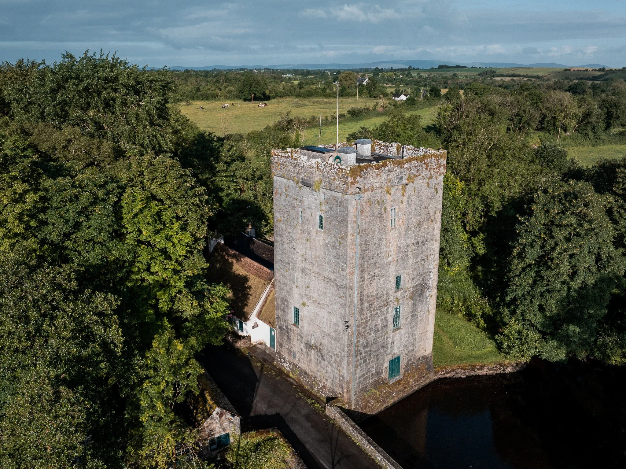 Close aerial view of the stone Yeats tower at Thoor Ballylee near Gort, County Galway, with its battlemented top, surrounding water and walls, and green farmland beyond