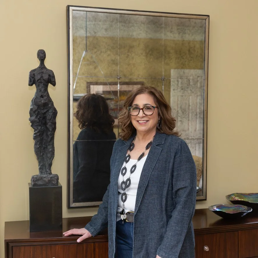 Woman standing beside a modern sculpture in a room with a large mirror and decorative bowls.