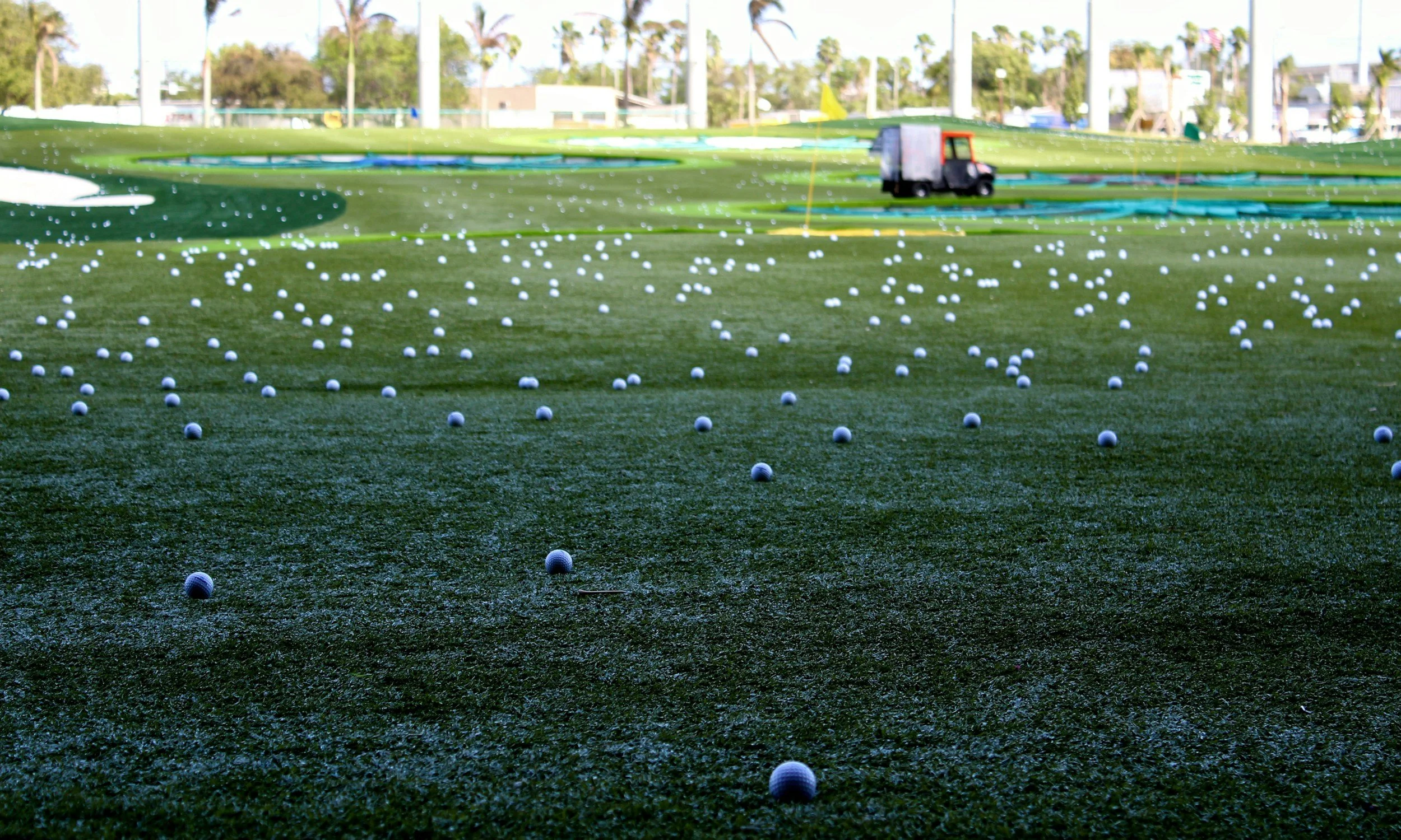Driving range field covered with scattered golf balls and a ball picker cart in the distance, illustrating golf practice with high-quality balls.