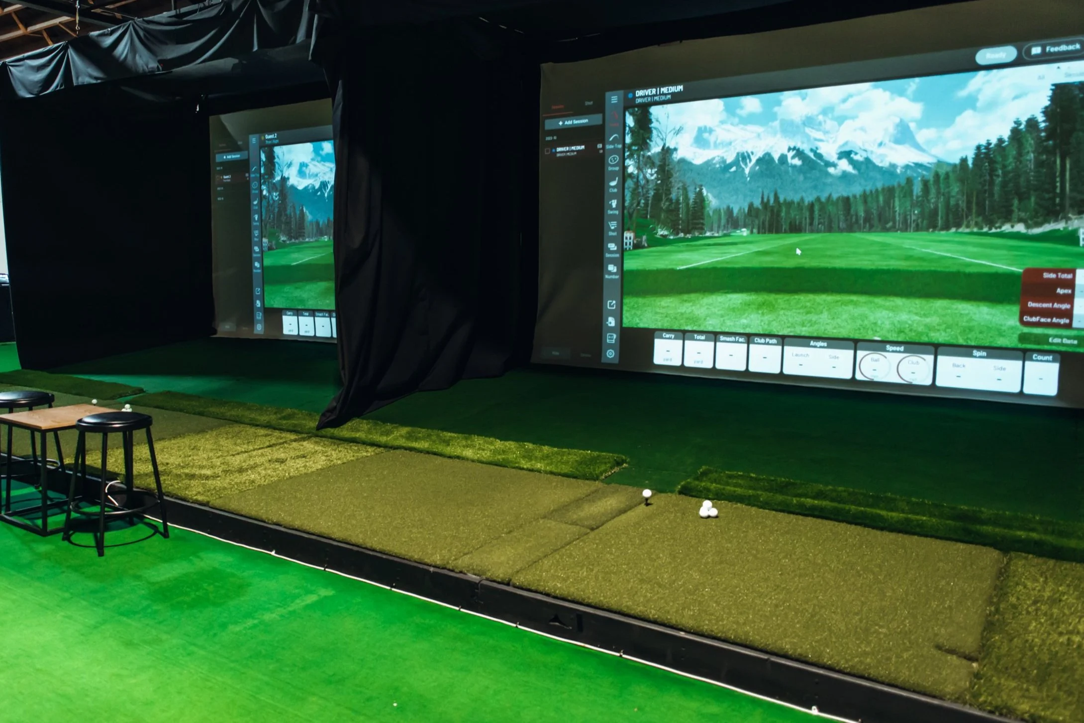 Indoor golf simulator with large screen display showing a virtual fairway, green hitting mats, and golf balls placed for practice.