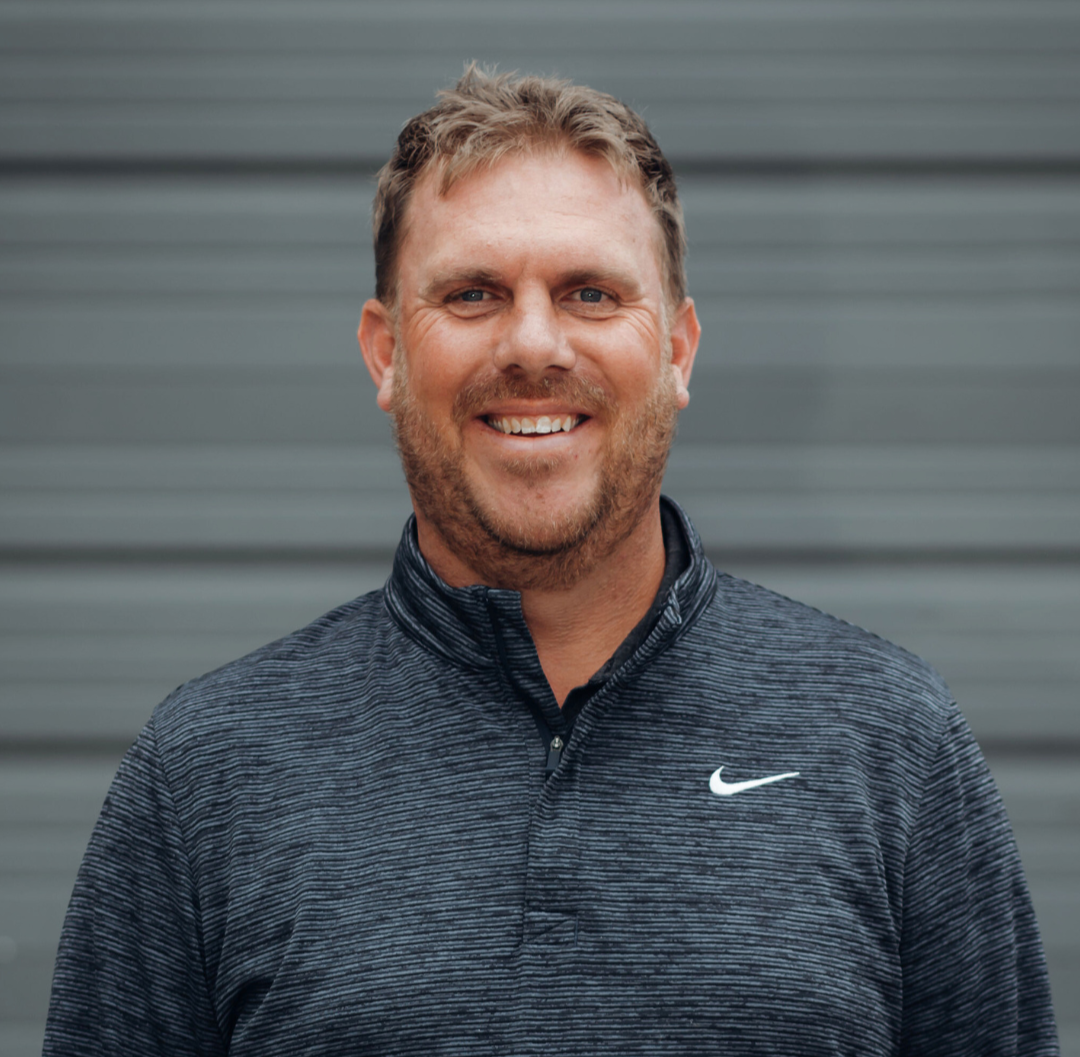 Brad Alston, Founder and PGA professional at Optimum Golf, smiling in front of a gray background. Experienced golf instructor in Denver specializing in strategy, technique, and mental discipline.