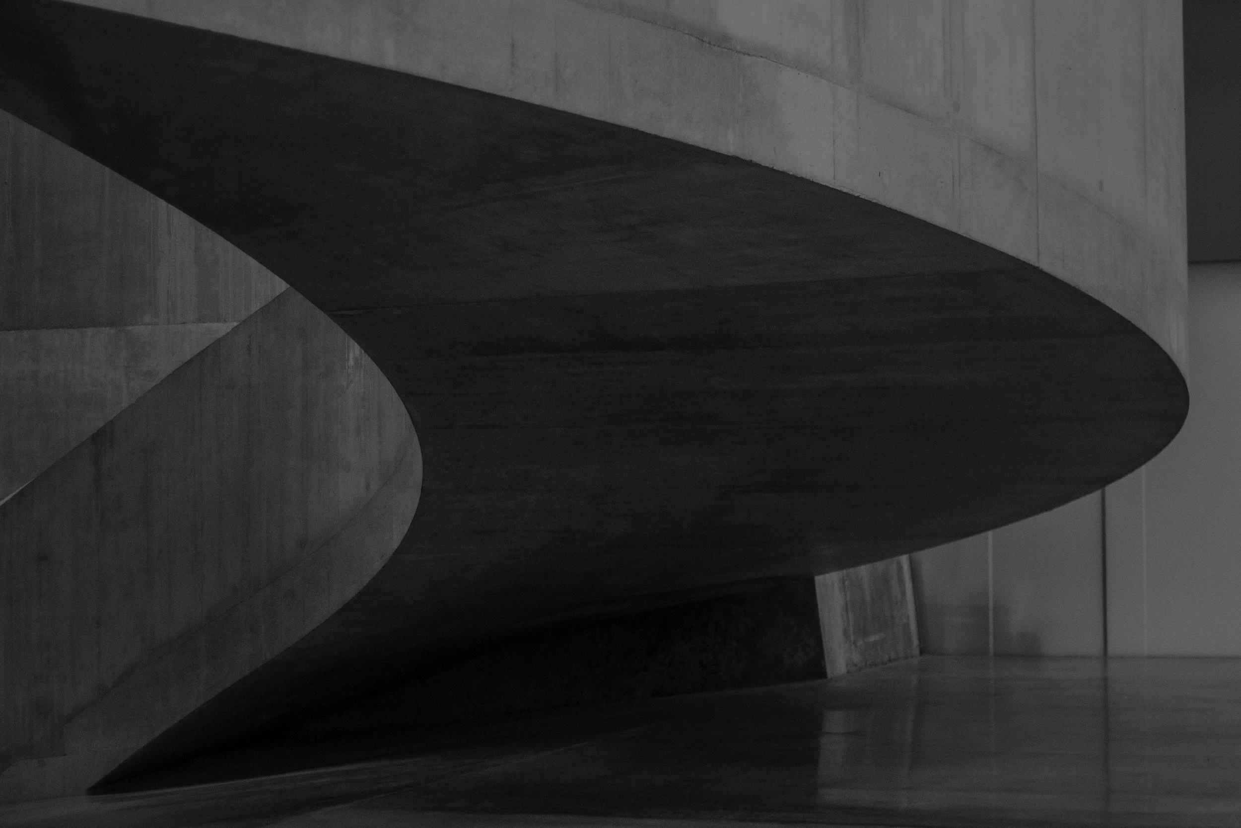 Black and white photograph of a modern, curved concrete staircase with smooth, rounded edges.