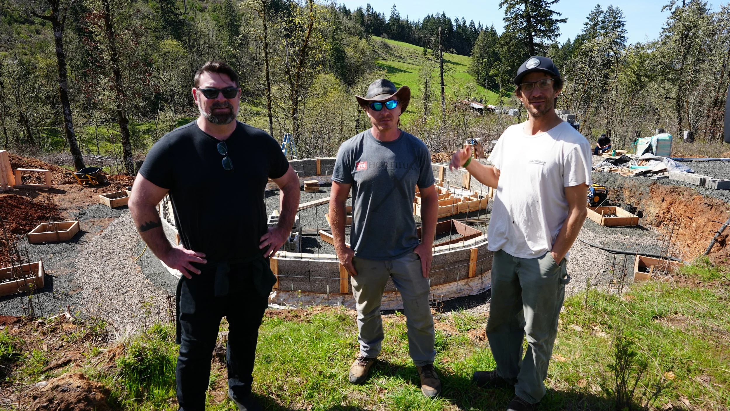 Three men smiling and giving thumbs up in front of circular home structure. 