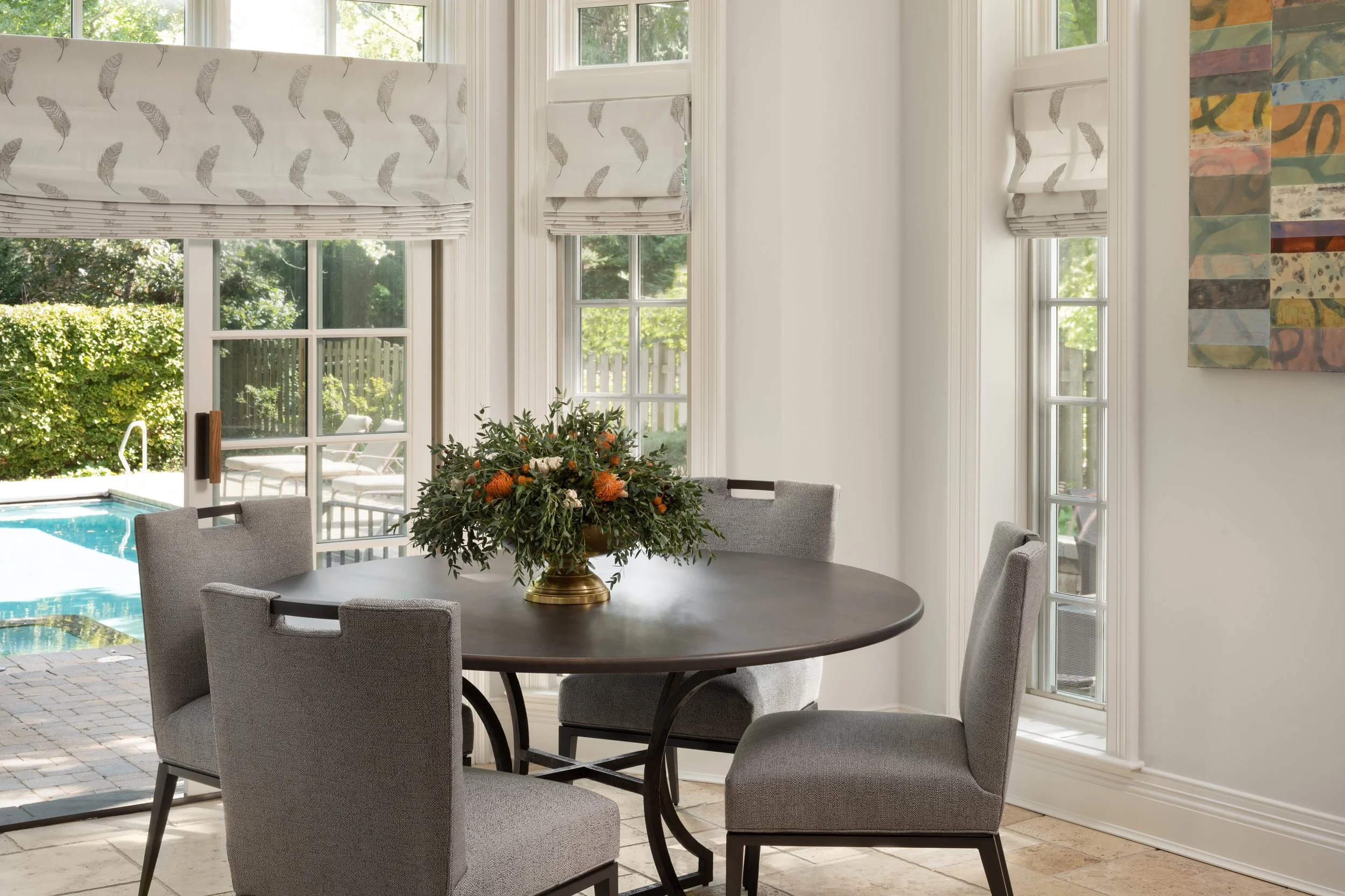 Modern living room with a fireplace, a dining table with vases and flowers, large windows, and built-in shelves with decorative items.
