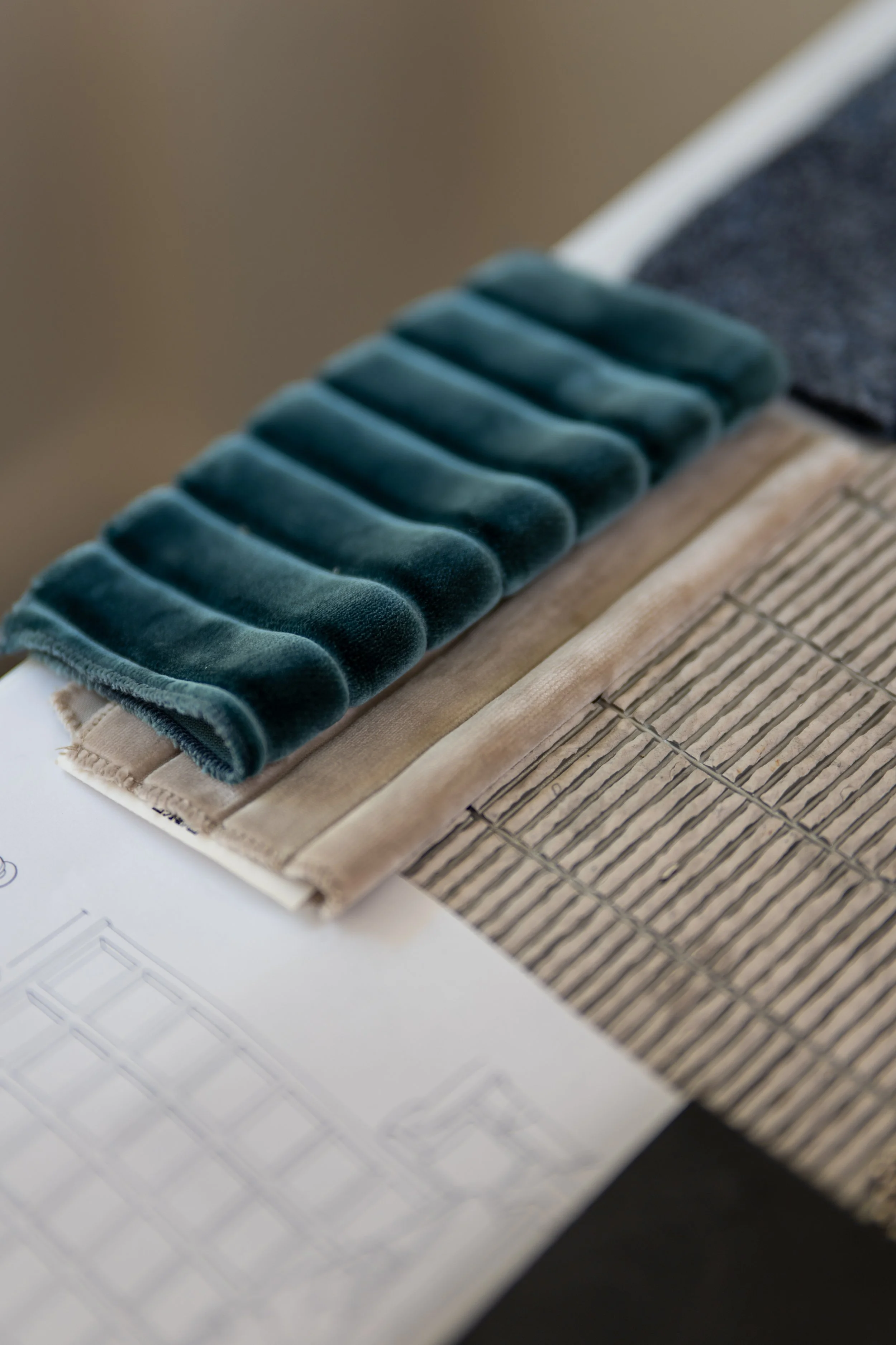 Close-up of a thread sample book with velvet fabric swatches in shades of green, beige, and dark navy, laid on a textured sample board.