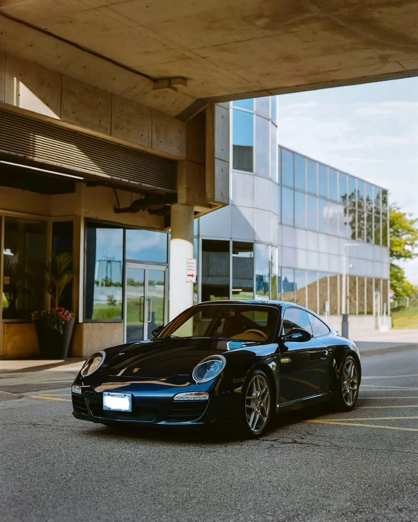 A black Porsche sports car parked in front of a modern glass building.