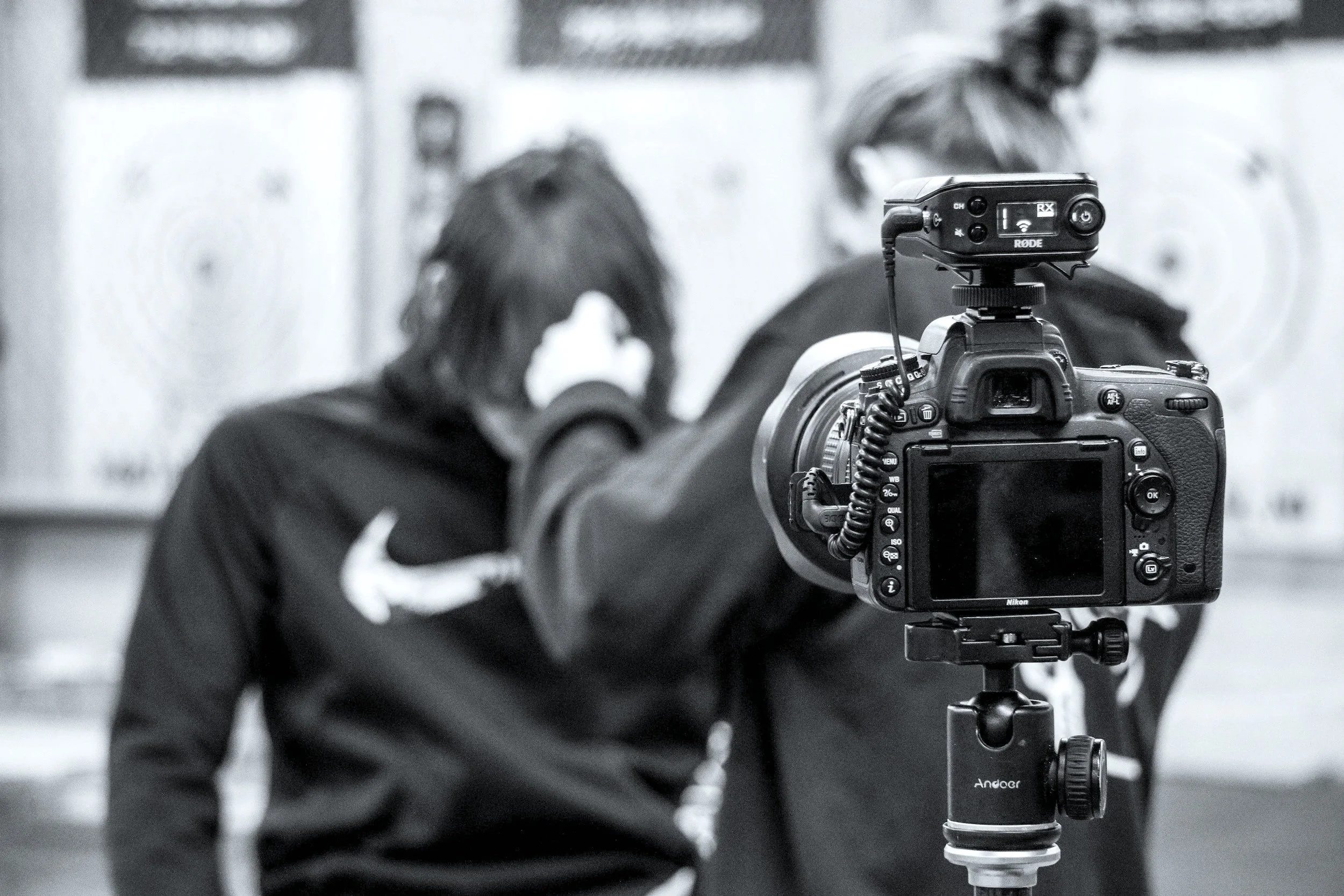 A DSLR camera mounted on a tripod, pointed at two individuals adjusting their headphones, with a blurred background.