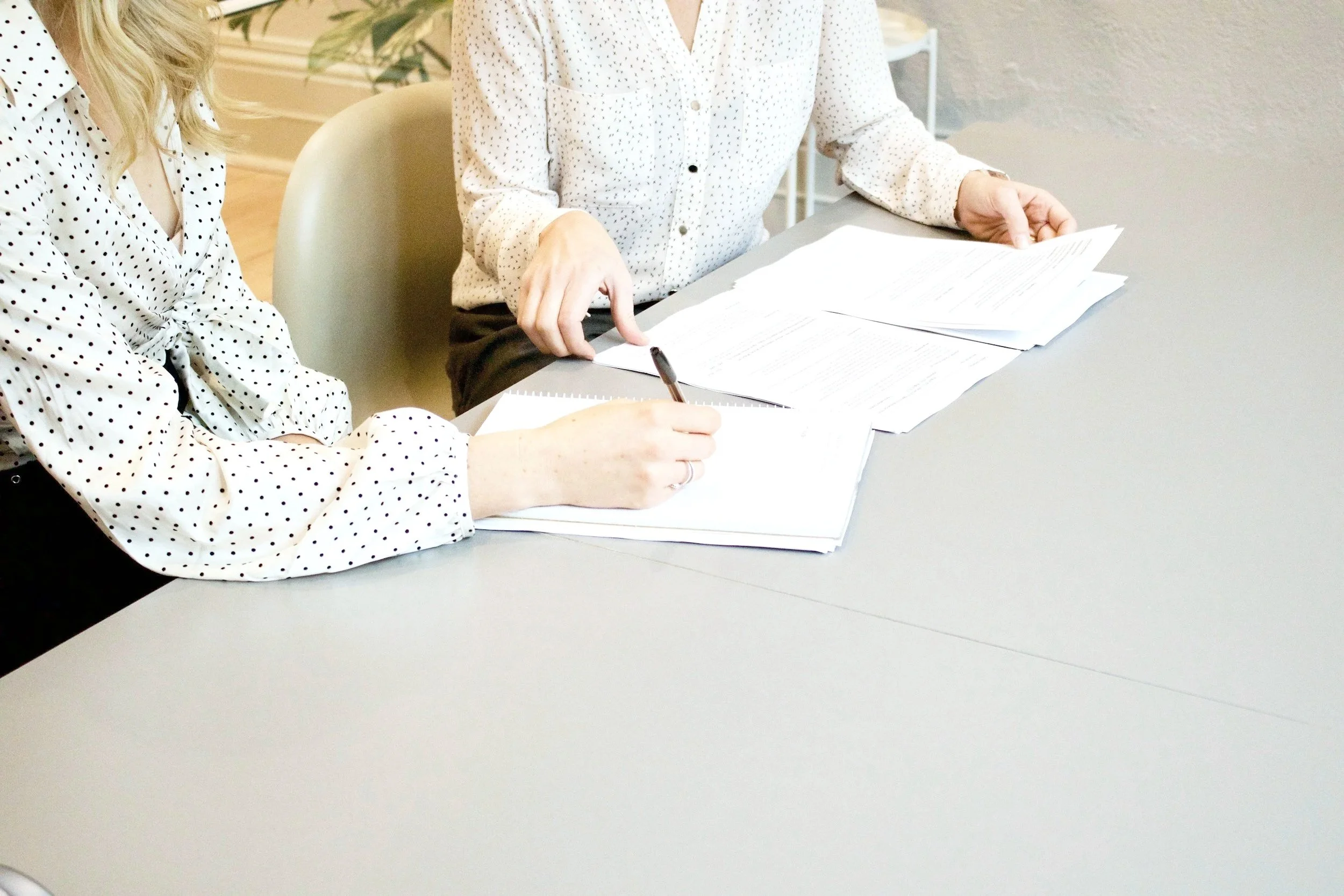 Two women reviewing and signing documents at a table in an office.
