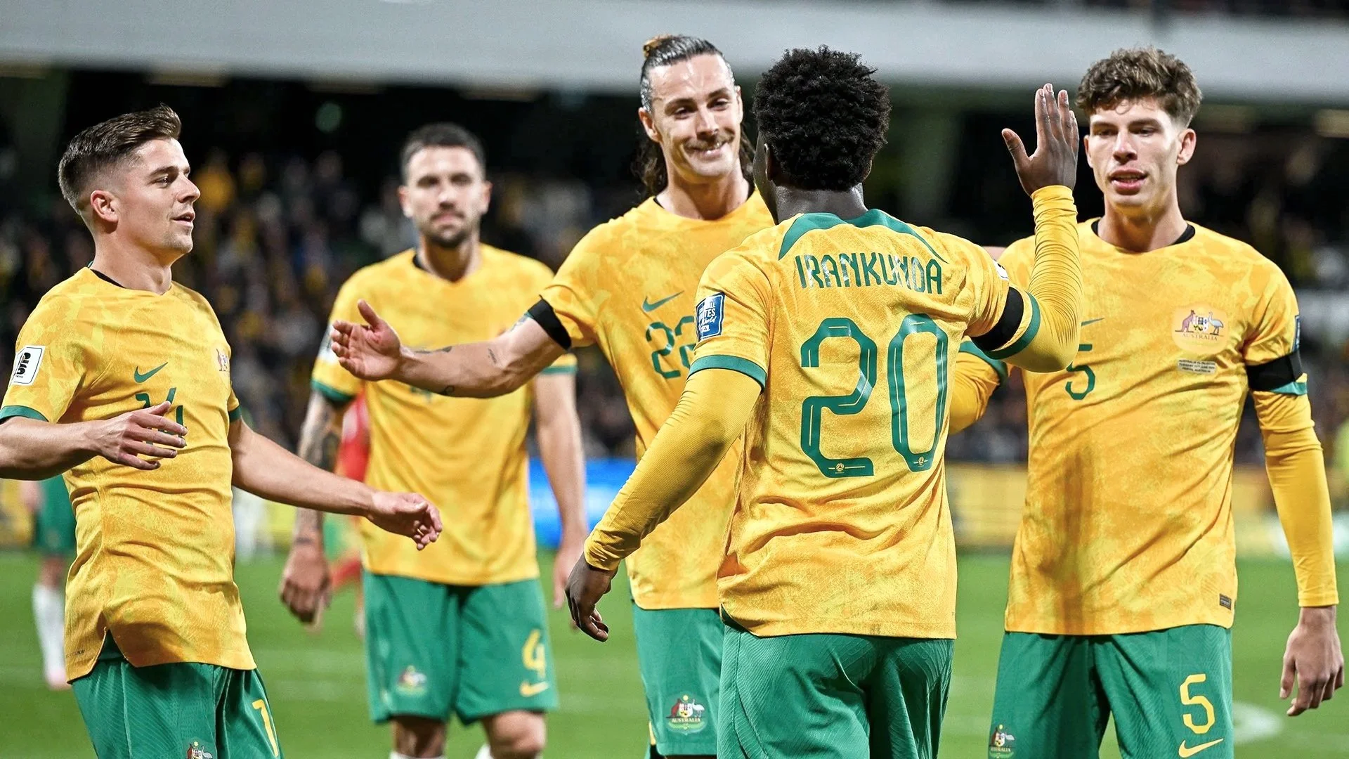 Australian men's soccer players celebrating on the field, wearing yellow jerseys and green shorts, during a match.
