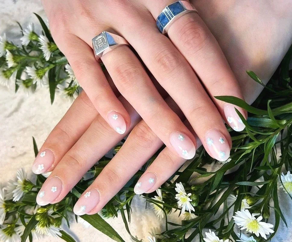 Chic and natural-looking nail design with a hint of sparkle, featuring transparent polish and delicate white flower accents – a signature nail art from River Nails and Spa, Great Falls, Virginia, for a touch of everyday sophistication.