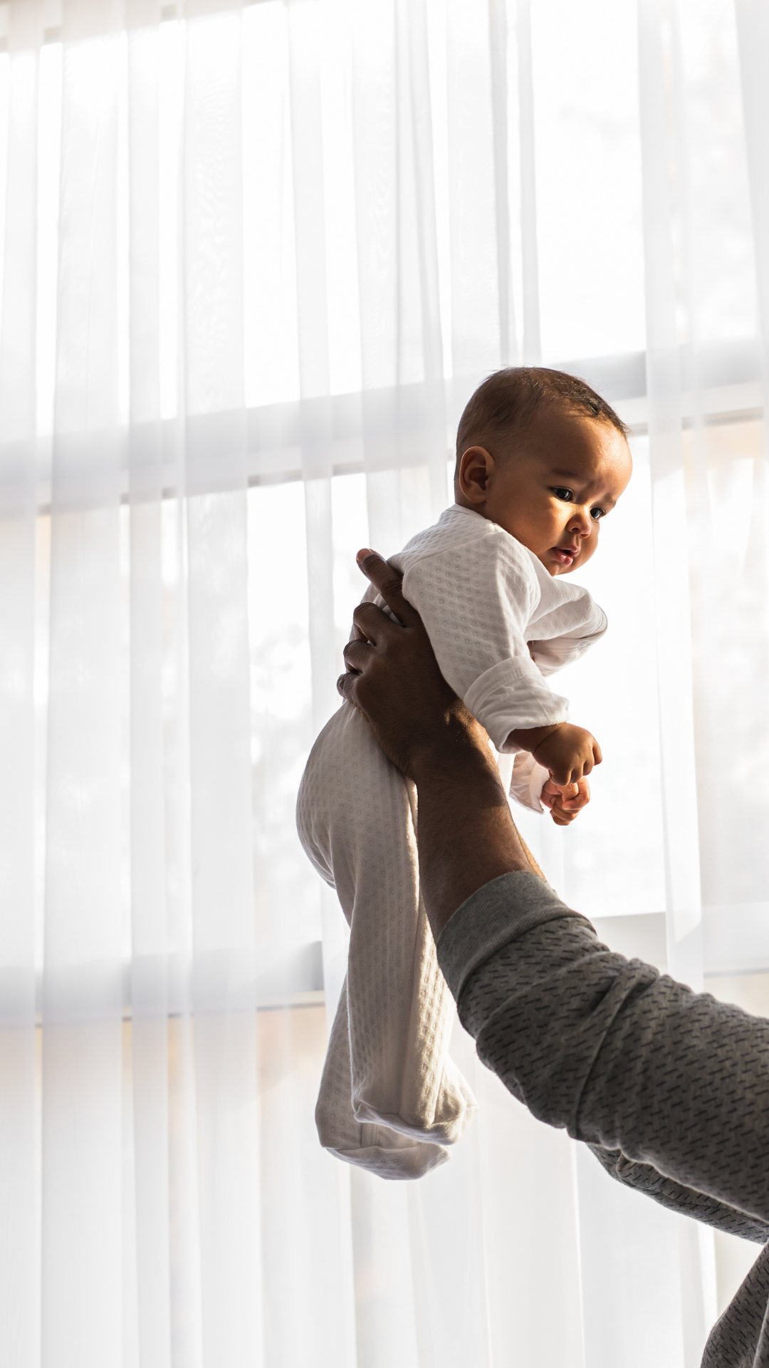 Mom holding baby in front of window in NYC home after visit from sleep coach and consultant