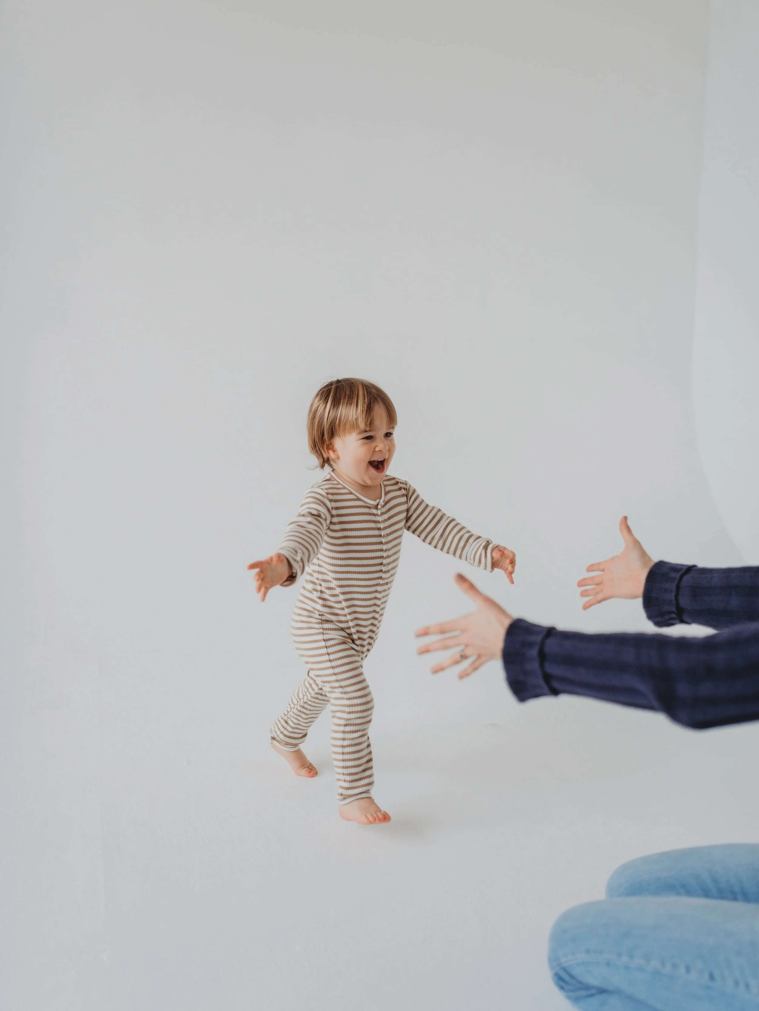 Baby walking towards sleep consultant in front of a white background