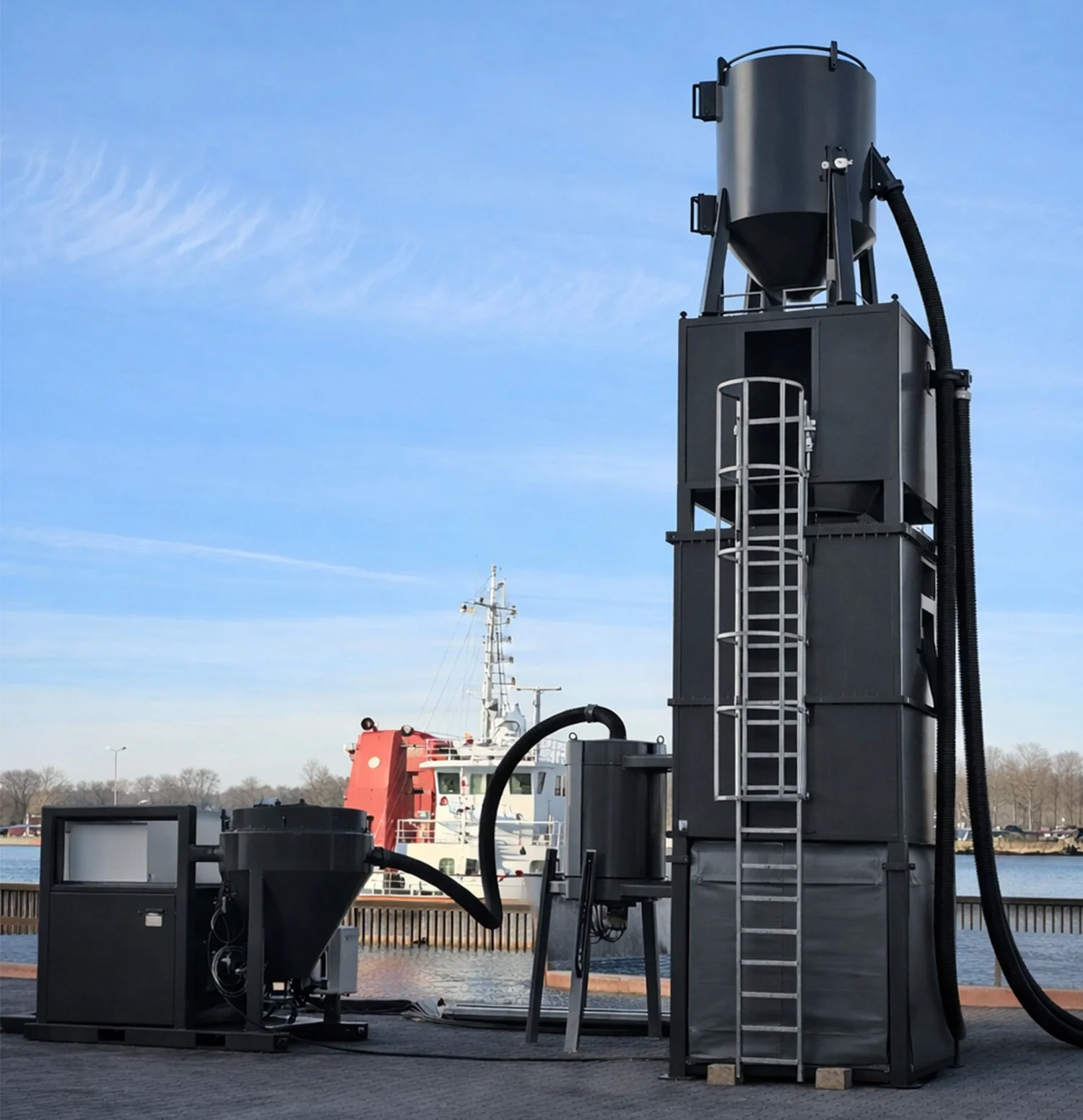 Industrial equipment near a body of water with a docked ship and blue sky in the background.