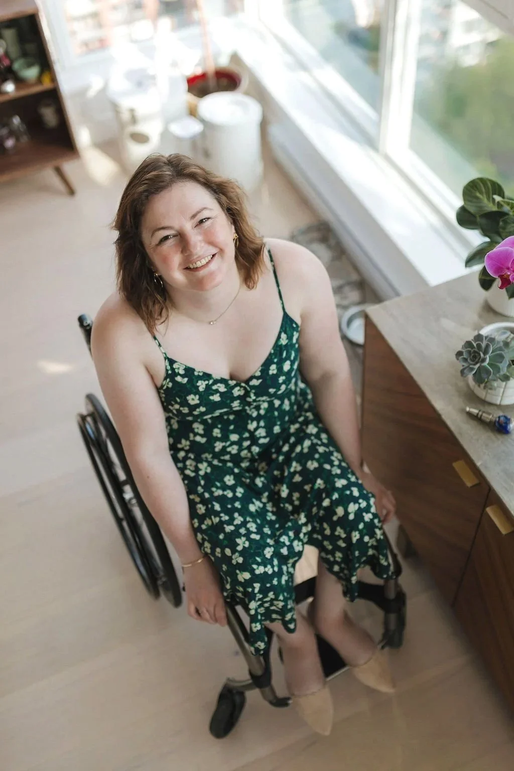 Ali sits in her wheelchair, smiling and looking up at the camera