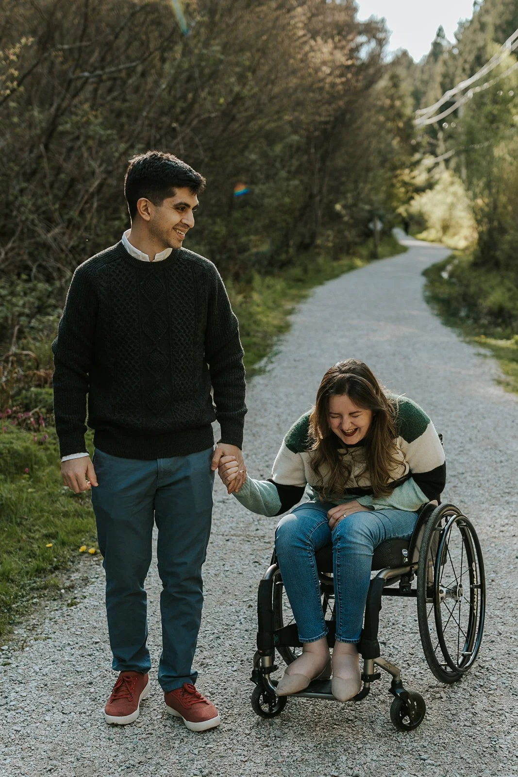 Ali is holding her husband's hand and bending over in her wheelchair, laughing