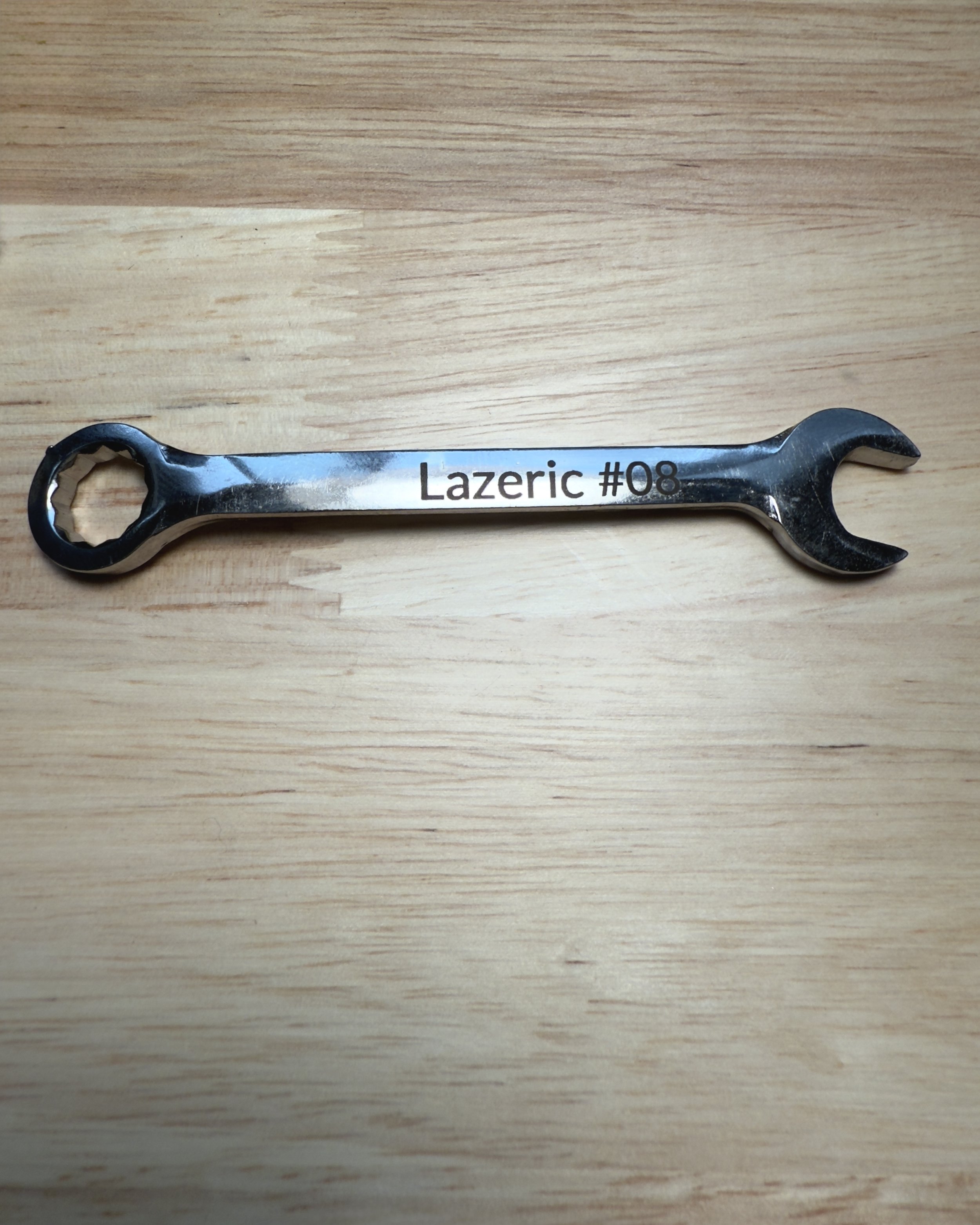 A chrome combination wrench engraved with the text “Lazeric #08” along the handle. The engraving is clean and dark, standing out against the polished metal surface, making it ideal for tool identification or branding. The wrench rests on a light wood