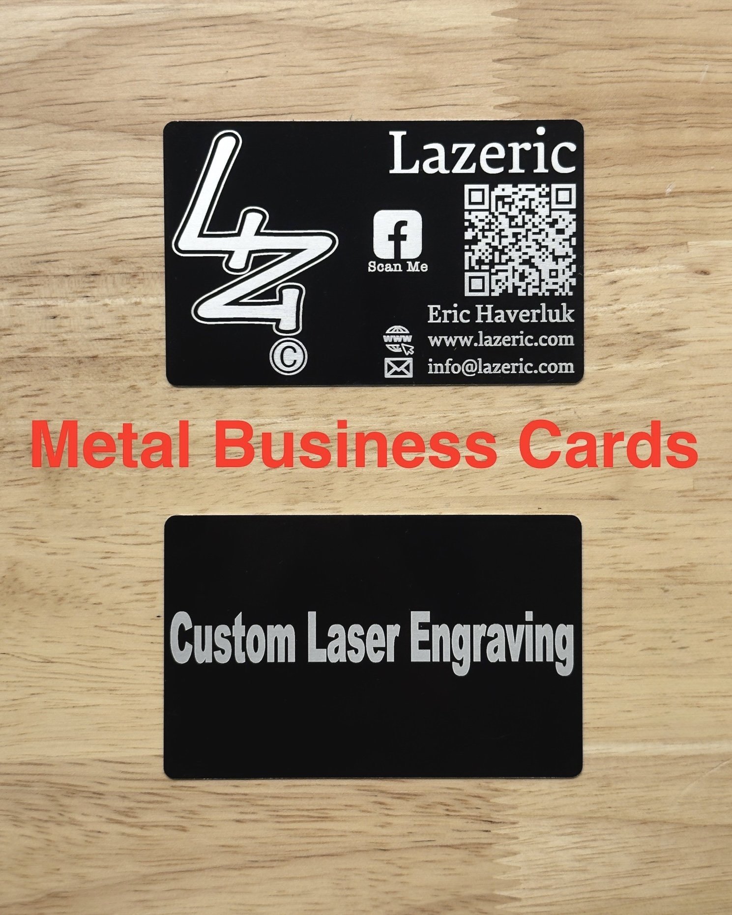 Two black metal business cards engraved with silver lettering are displayed on a wood surface. The top card features the Lazeric logo, contact info for Eric Haverluk, a QR code, and social media icons. The bottom card simply reads “Custom Laser Engra