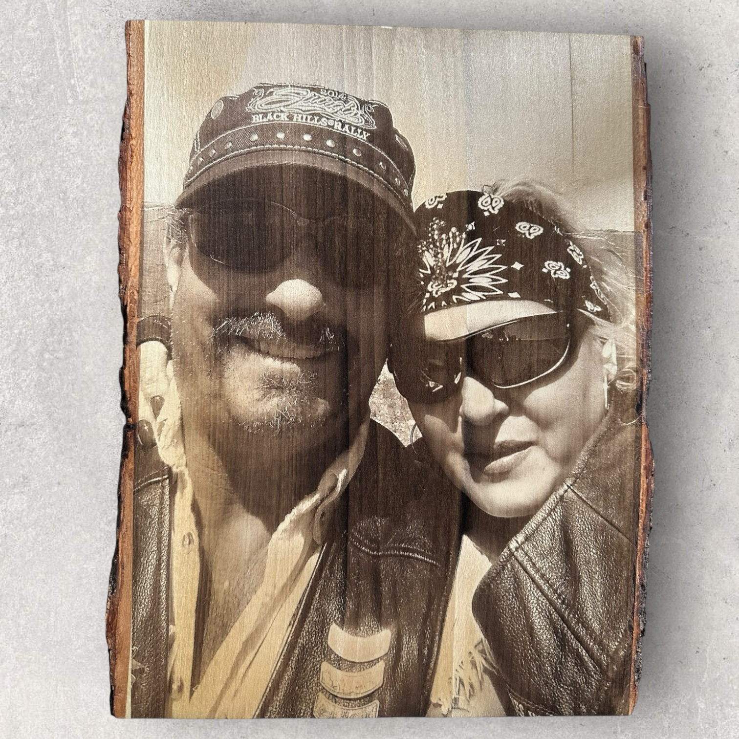 Laser engraved portrait of a biker couple wearing sunglasses on live edge wood with natural bark border