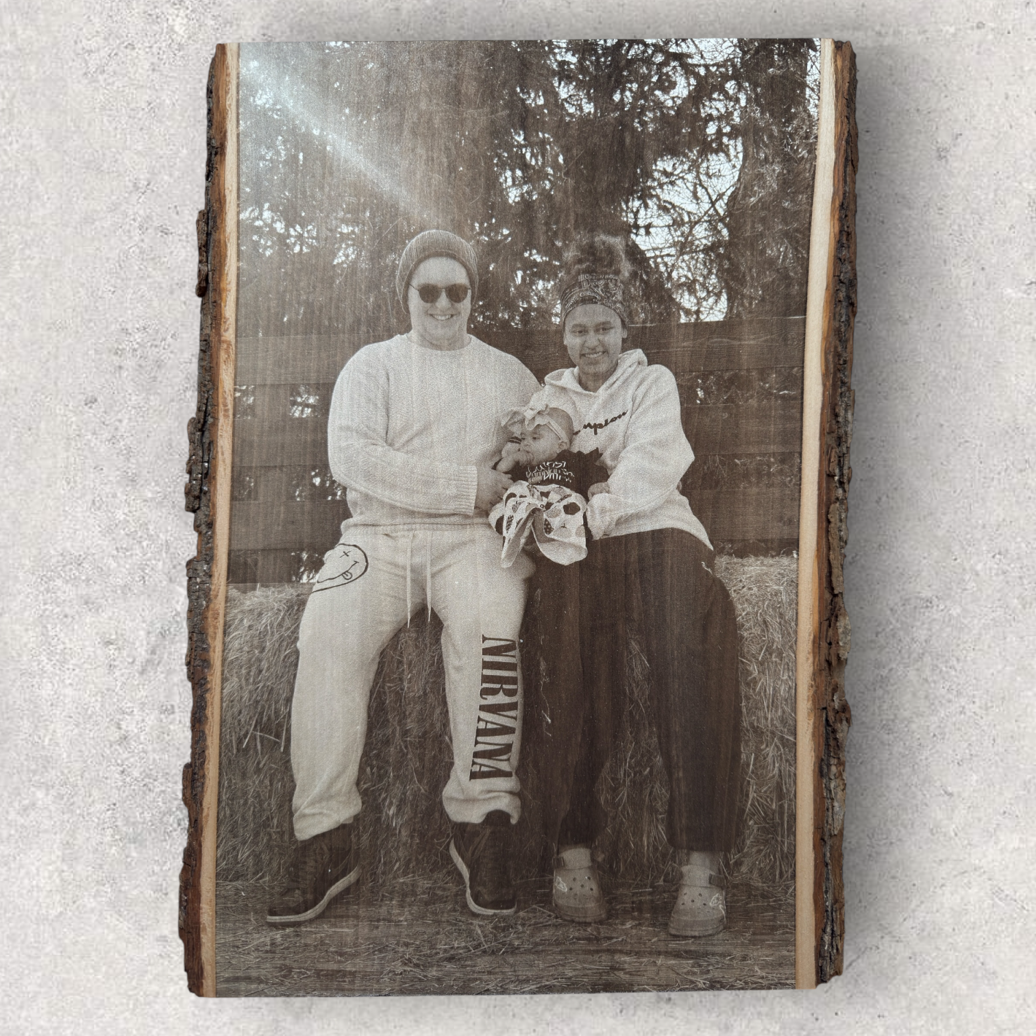 Laser engraved family photo on live edge wood showing parents holding a baby while seated on hay bales