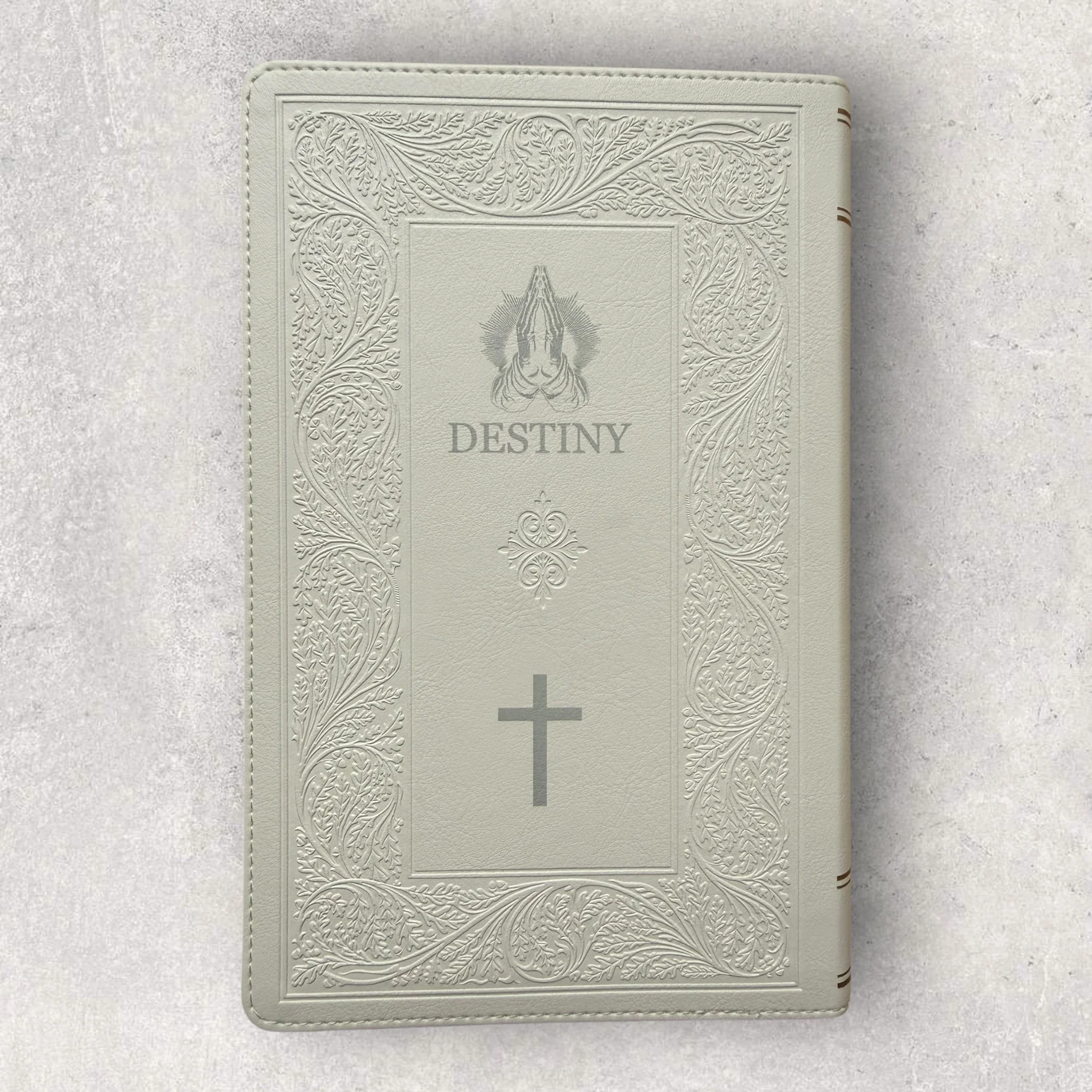 Custom laser-engraved Bible with light-colored leather cover, detailed embossed border, praying hands graphic, and cross symbol on the front, engraved by Lazeric for personalized religious keepsakes.