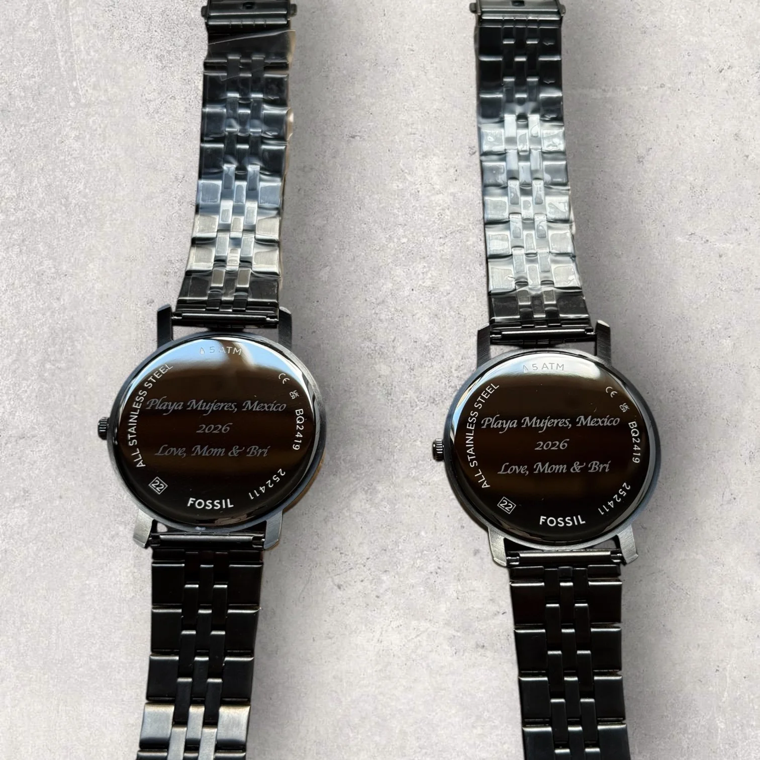Two Fossil stainless steel watches with custom laser-engraved case backs reading “Playa Mujeres, Mexico 2026 – Love, Mom & Bri,” personalized as a commemorative gift.