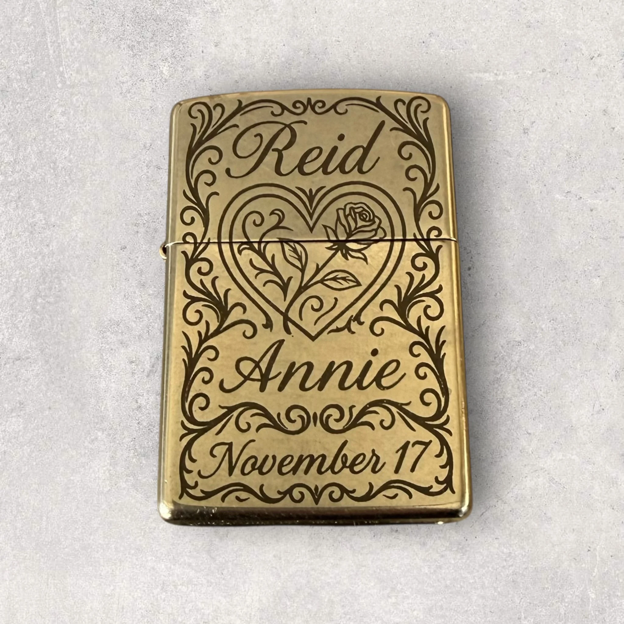 Custom laser-engraved brass lighter with decorative floral design, names, and date, showcasing detailed personalized metal engraving for a keepsake gift.