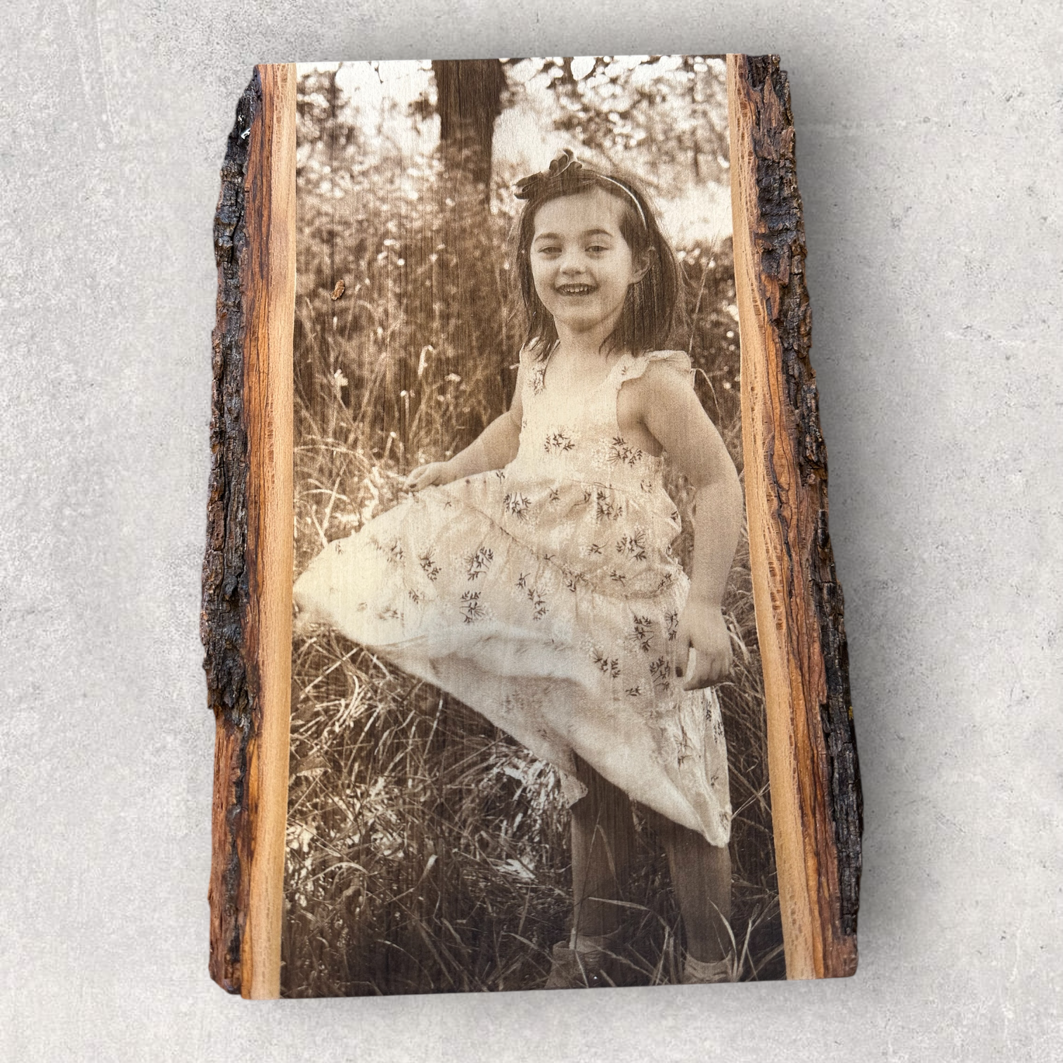 Rustic photo engraving of a girl in a floral dress smiling in a field, on bark-edged hardwood slab