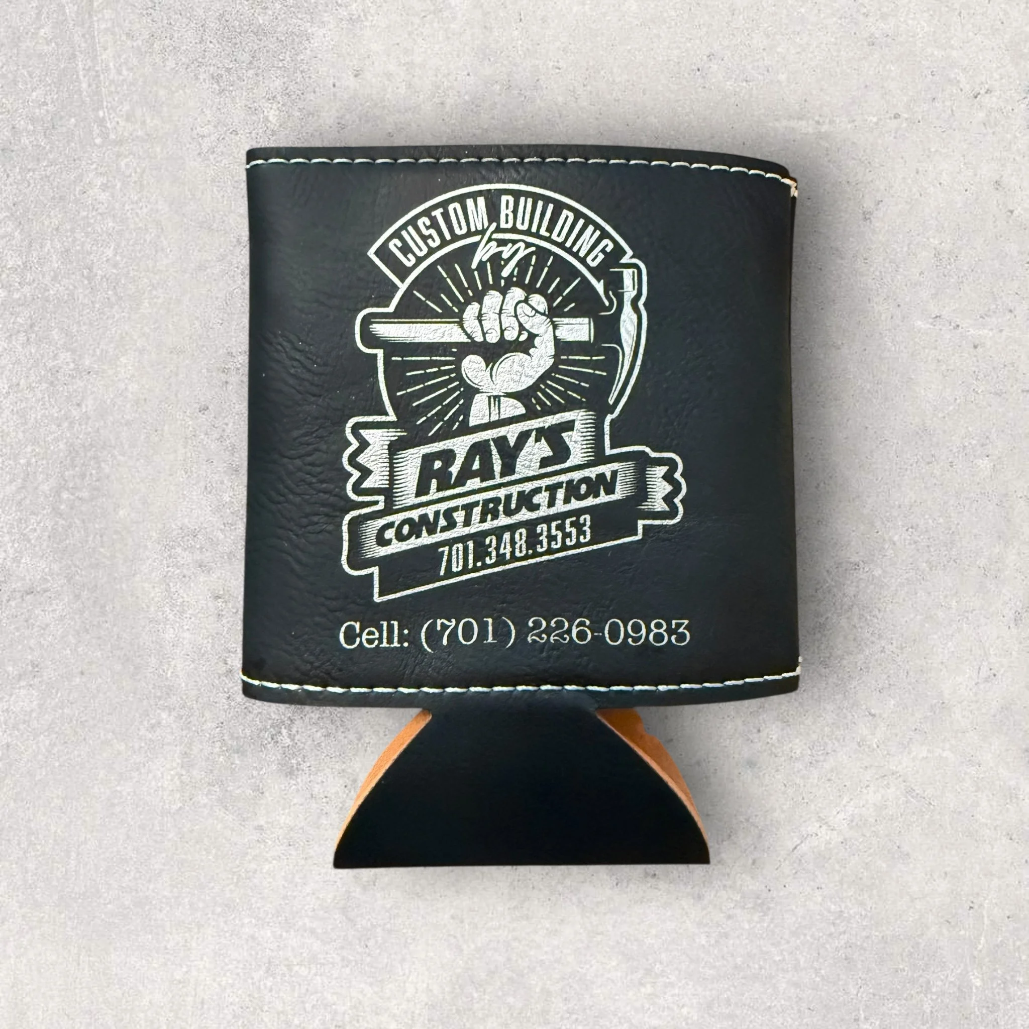 Custom laser-engraved black leather can koozie with the Ray’s Construction logo and contact information, showcasing detailed branding and professional laser engraving.