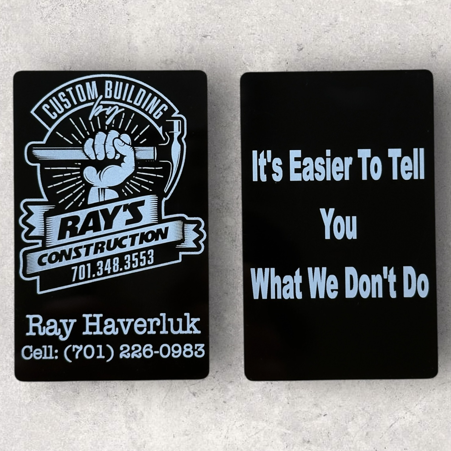 Laser engraved business cards for Ray's Construction with detailed logo and bold slogan on black metal finish - Lazeric