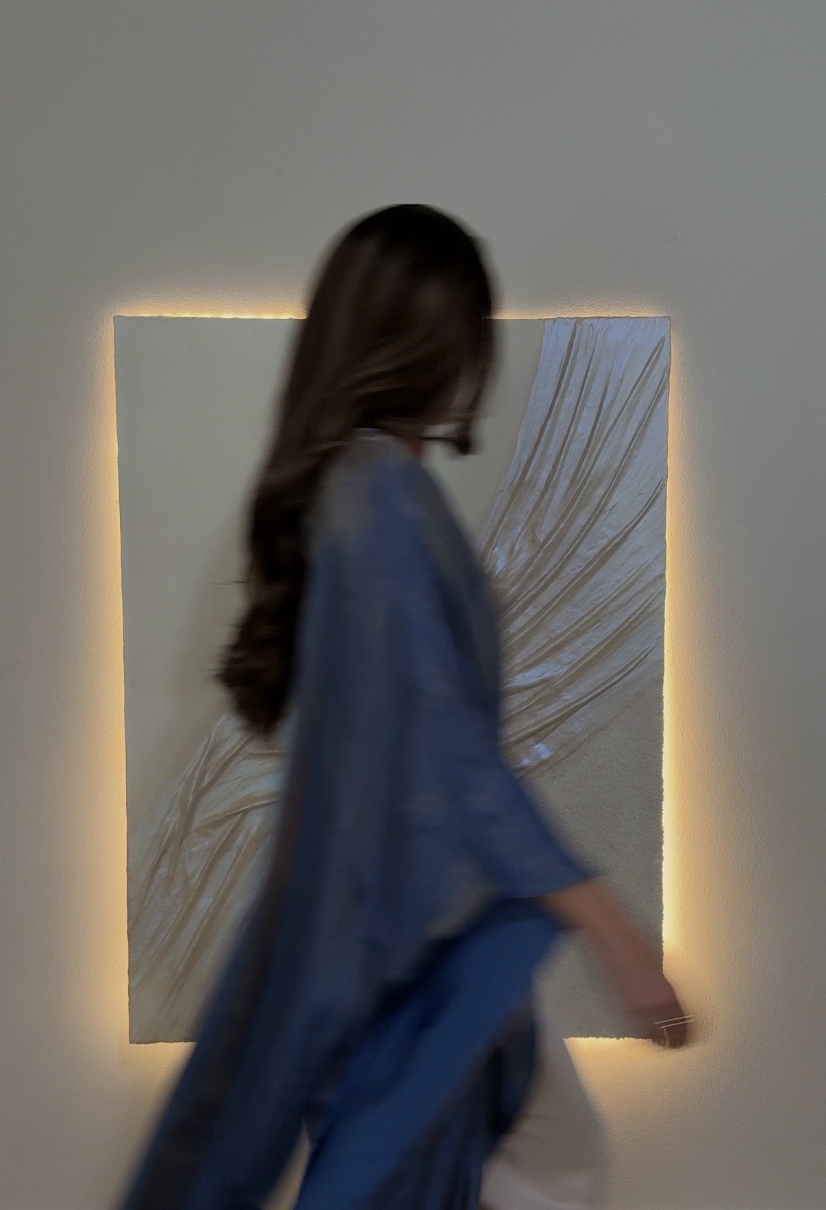 Ripple & Roam artist walking in front of an illuminated oyster-inspired sculptural painting with dimensional white texture.