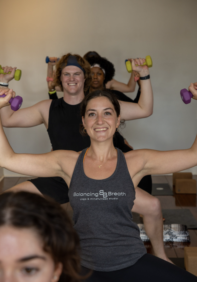 Group of people practicing yoga in a studio with an exposed brick wall, high ceiling, and large black ventilation pipes.