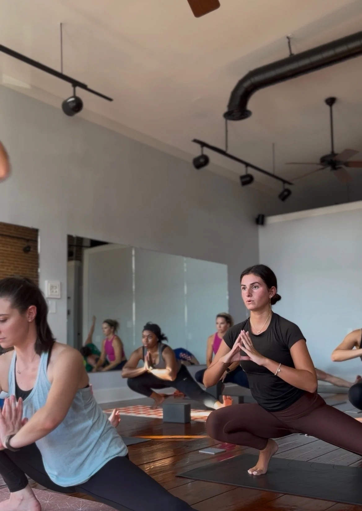 People practicing yoga in a studio with wooden floors and brick walls.