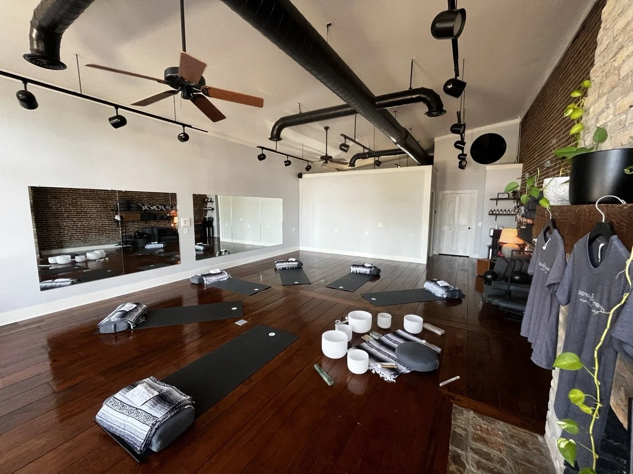 Person in white clothing arranging or playing singing bowls on a wooden floor.