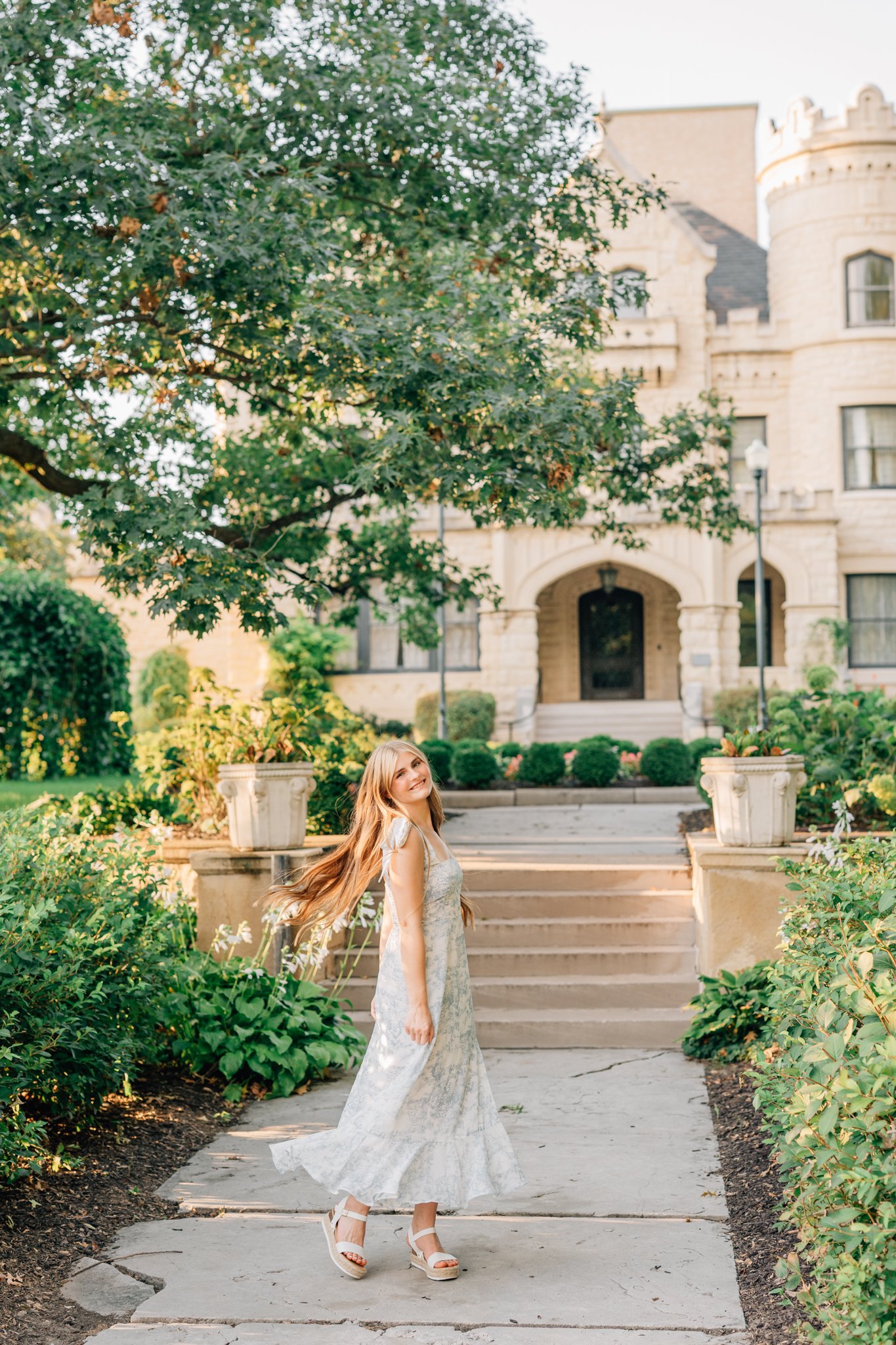 Girl in long white dress twirls in front of Jocelyn Castle for her senior pictures in Omaha.