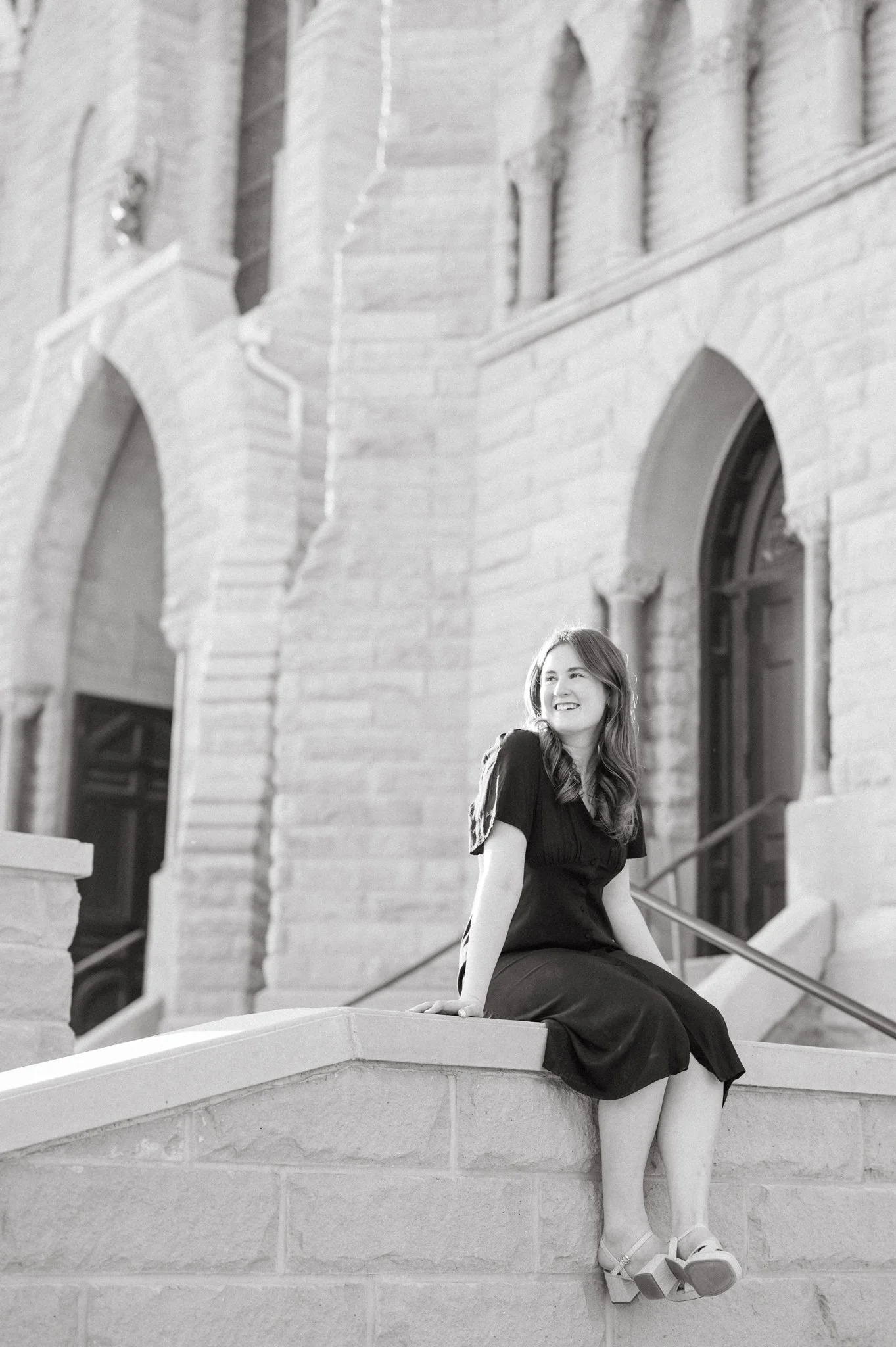 Black and white photo of girl sitting on ledge at St. John's church on Creighton's campus during her college graduation photography session.