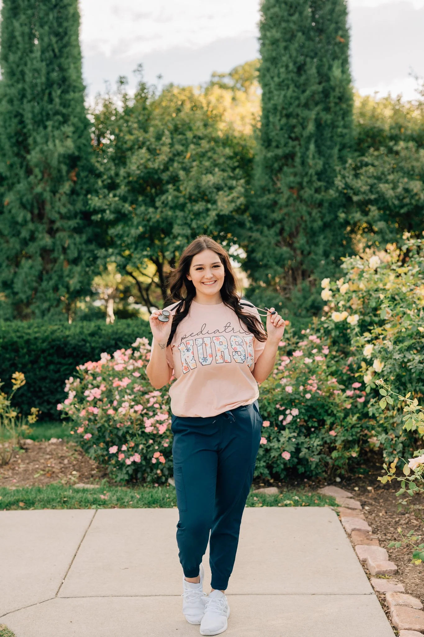 Nursing graduate poses in scrubs with stethoscope for her graduation photos in Omaha.