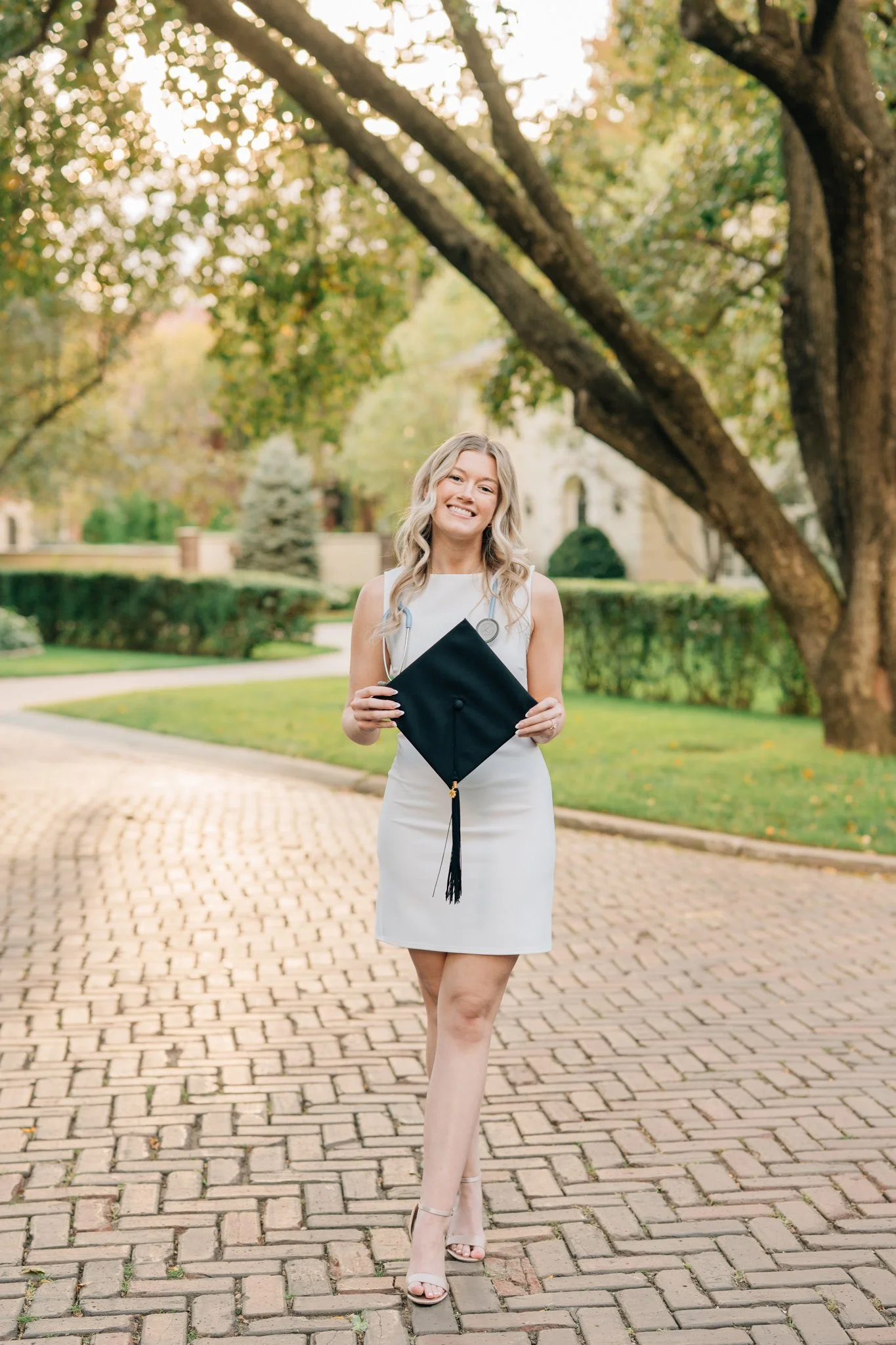 Nursing graduate in white dress poses with graduation cap to celebrate graduating from Nebraska Methodist during grad photo session.