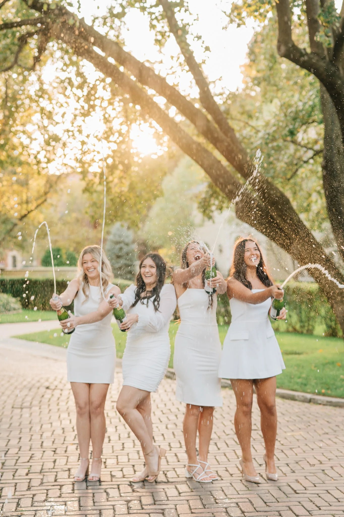 Four Nebraska Methodist nursing grads in white dresses laugh while popping champagne during senior photos in Omaha.