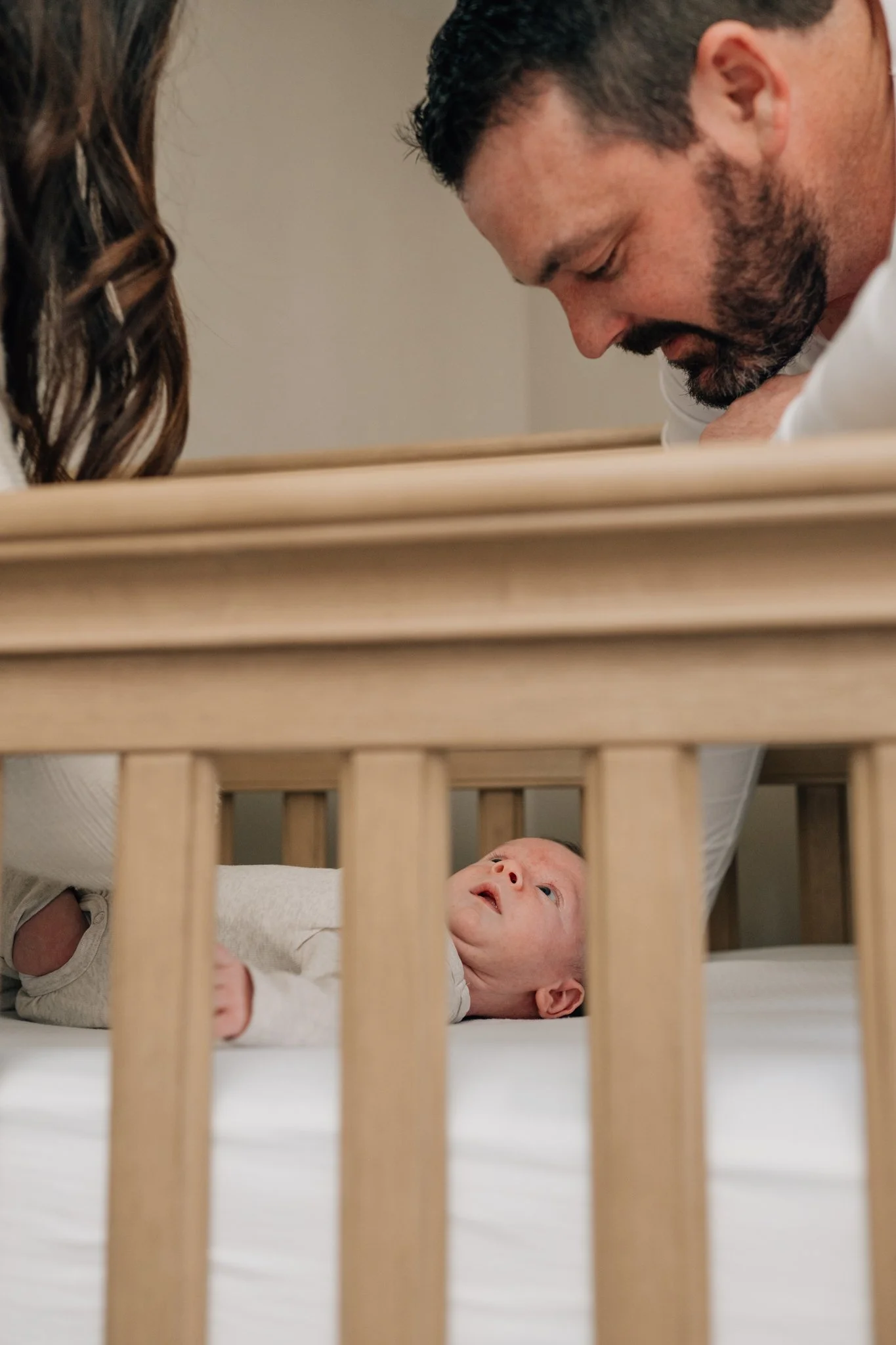 Dad looks down into crib as his newborn son looks up at him during in home lifestyle newborn session in Iowa.