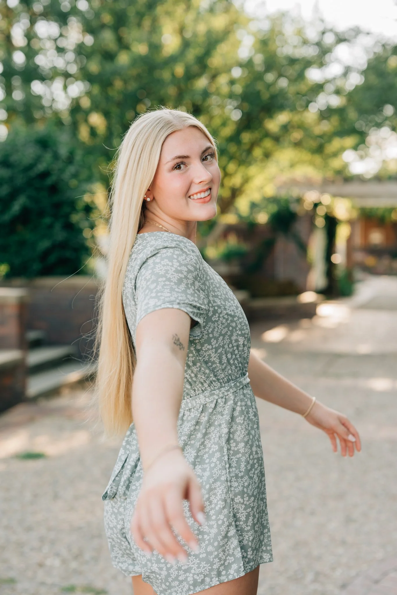 Girl reaches back for the camera as she walks away during golden hour during her senior pictures in Omaha.